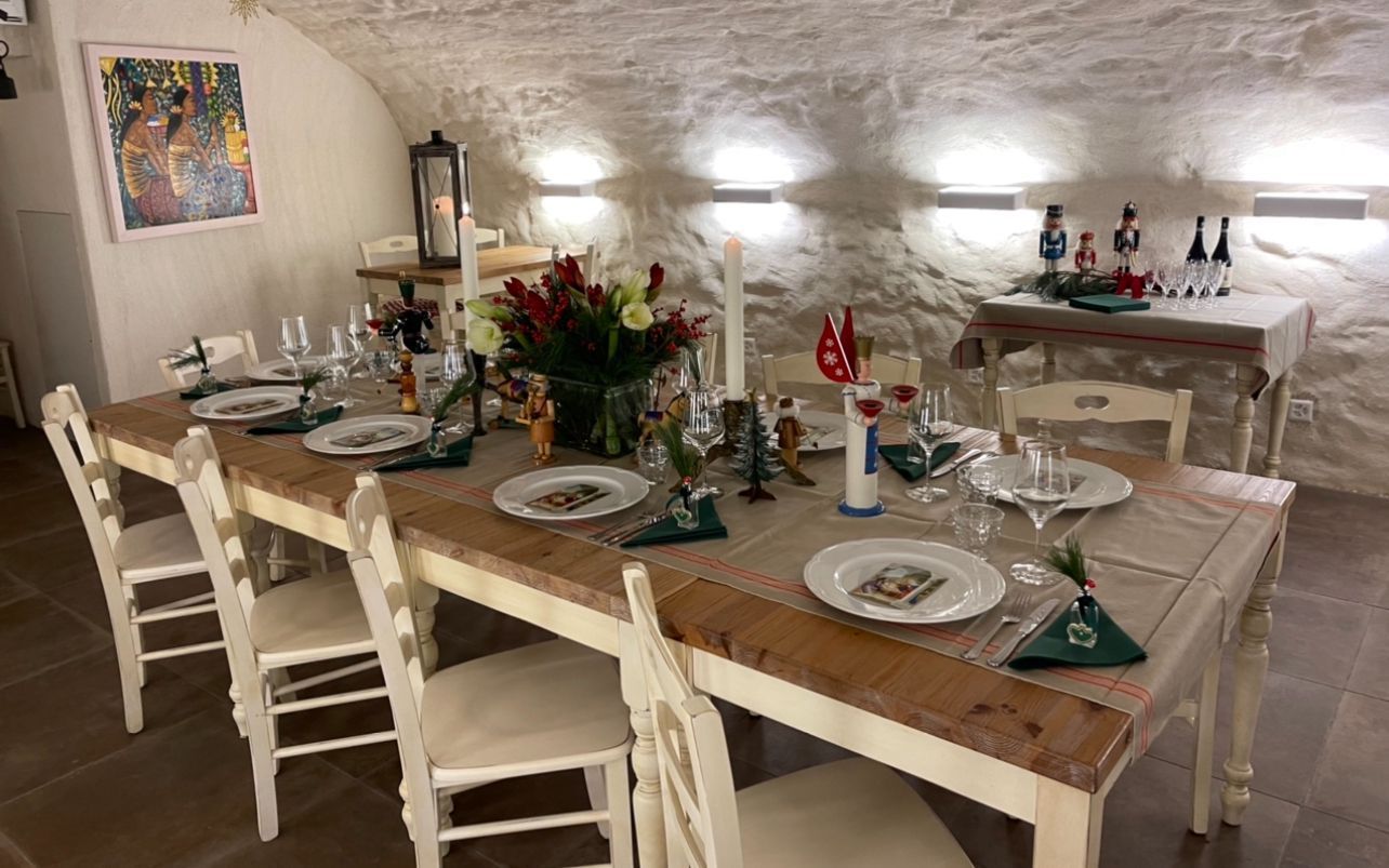 Ein langer Esstisch aus Holz, gedeckt für ein formelles Abendessen, in einem Raum mit steinernen Bogenwänden und beleuchteten Wandleuchten.