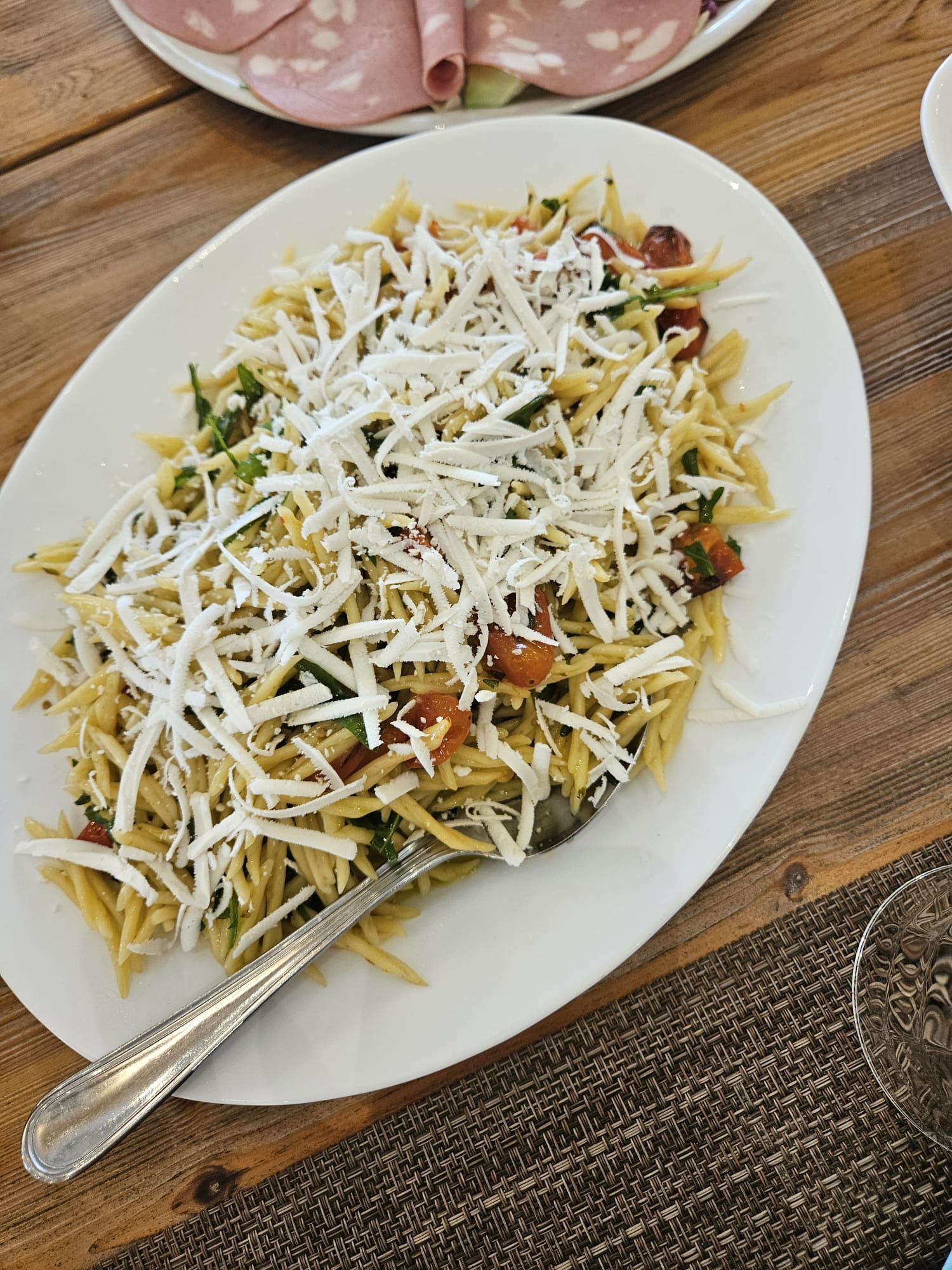Eine weiße, ovale Platte mit Orzo-Nudeln, Kirschtomaten und frischen Kräutern, großzügig mit geriebenem Käse bestreut.