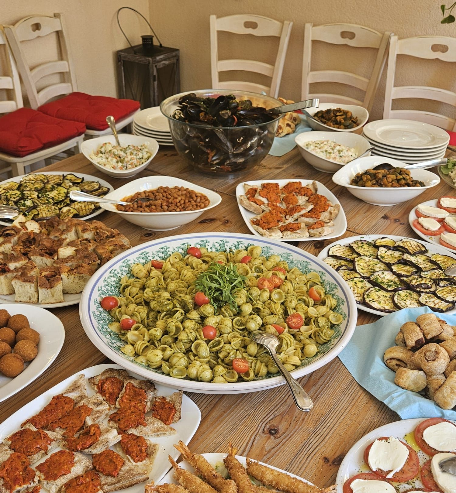 Ein rustikaler Holztisch ist für eine Dinnerparty mit einer Auswahl an Vorspeisen, Nudelsalaten und geröstetem Gemüse gedeckt.