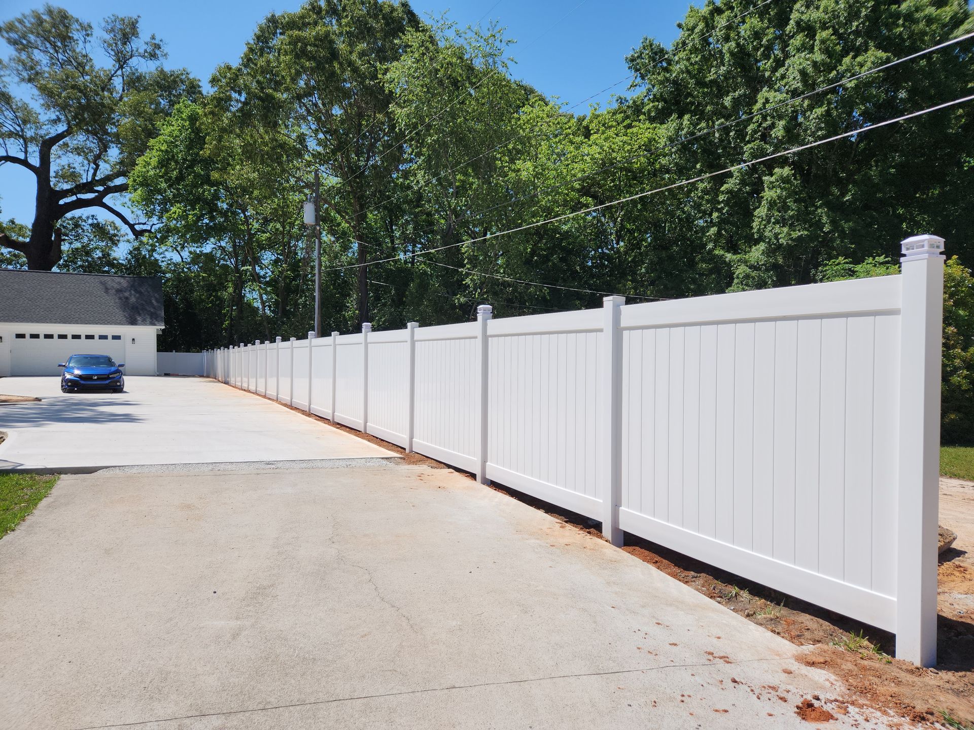 A white fence is along the side of a driveway