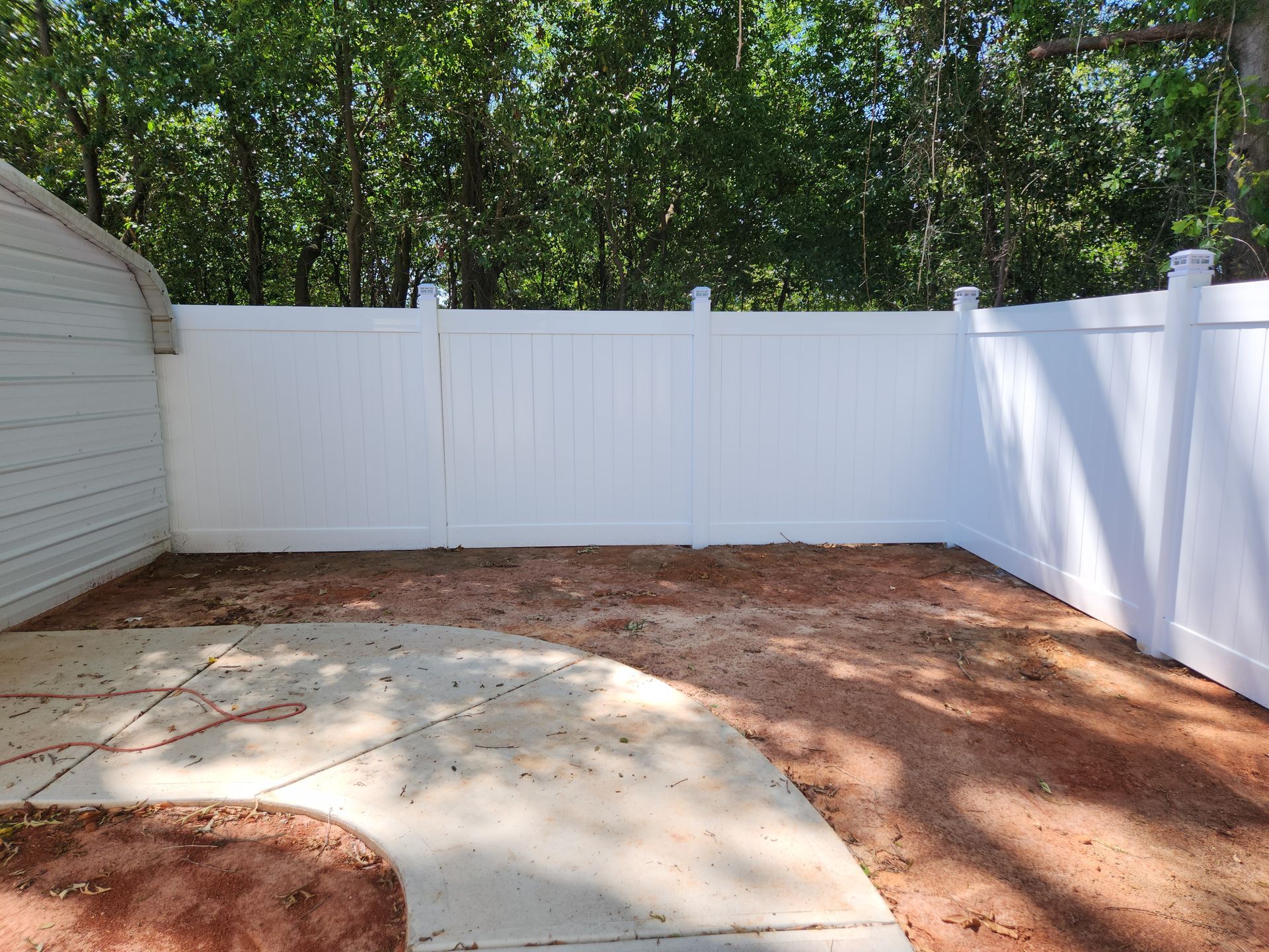 An empty backyard with a white fence and trees in the background.