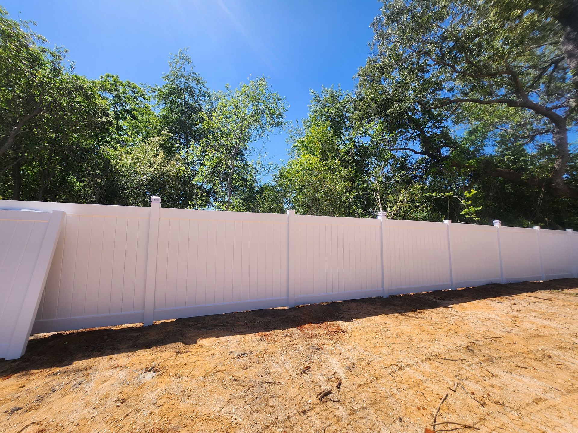 A white fence surrounds a dirt field with trees in the background.