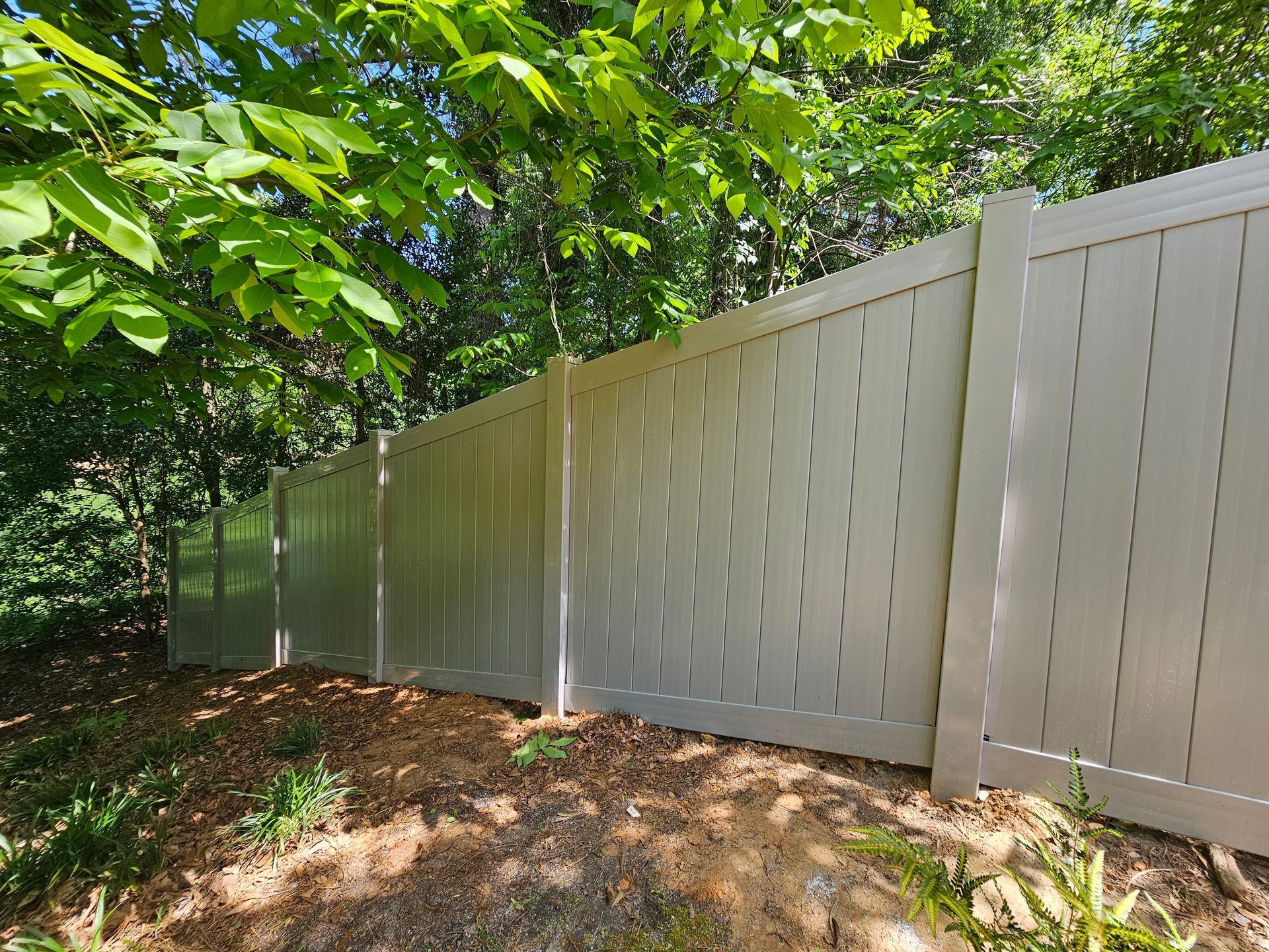 A white fence is surrounded by trees in a backyard.