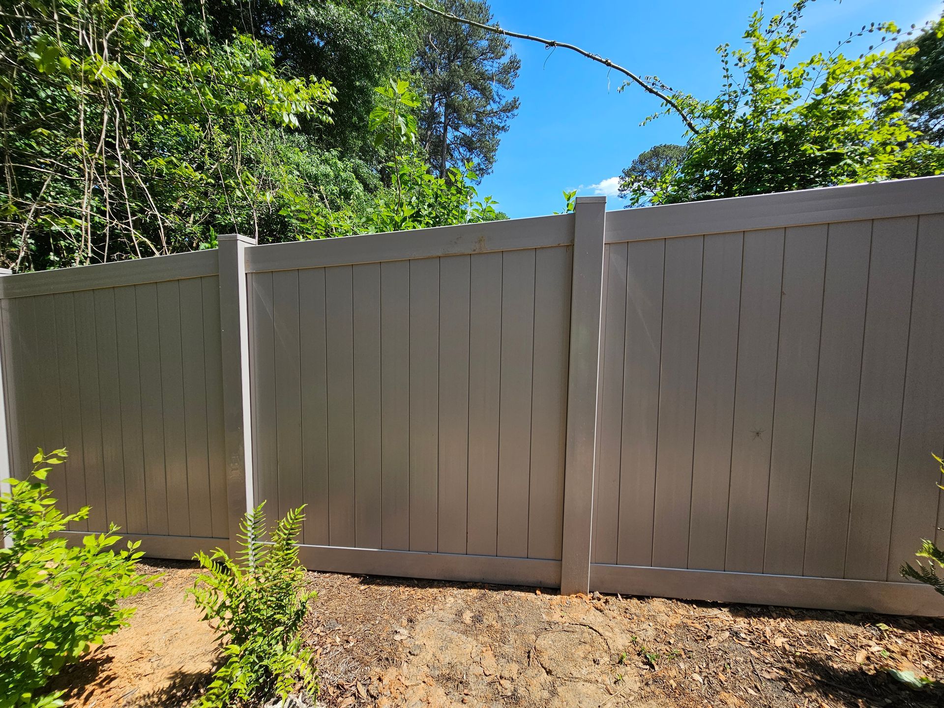 A white fence is surrounded by trees and dirt in a yard.