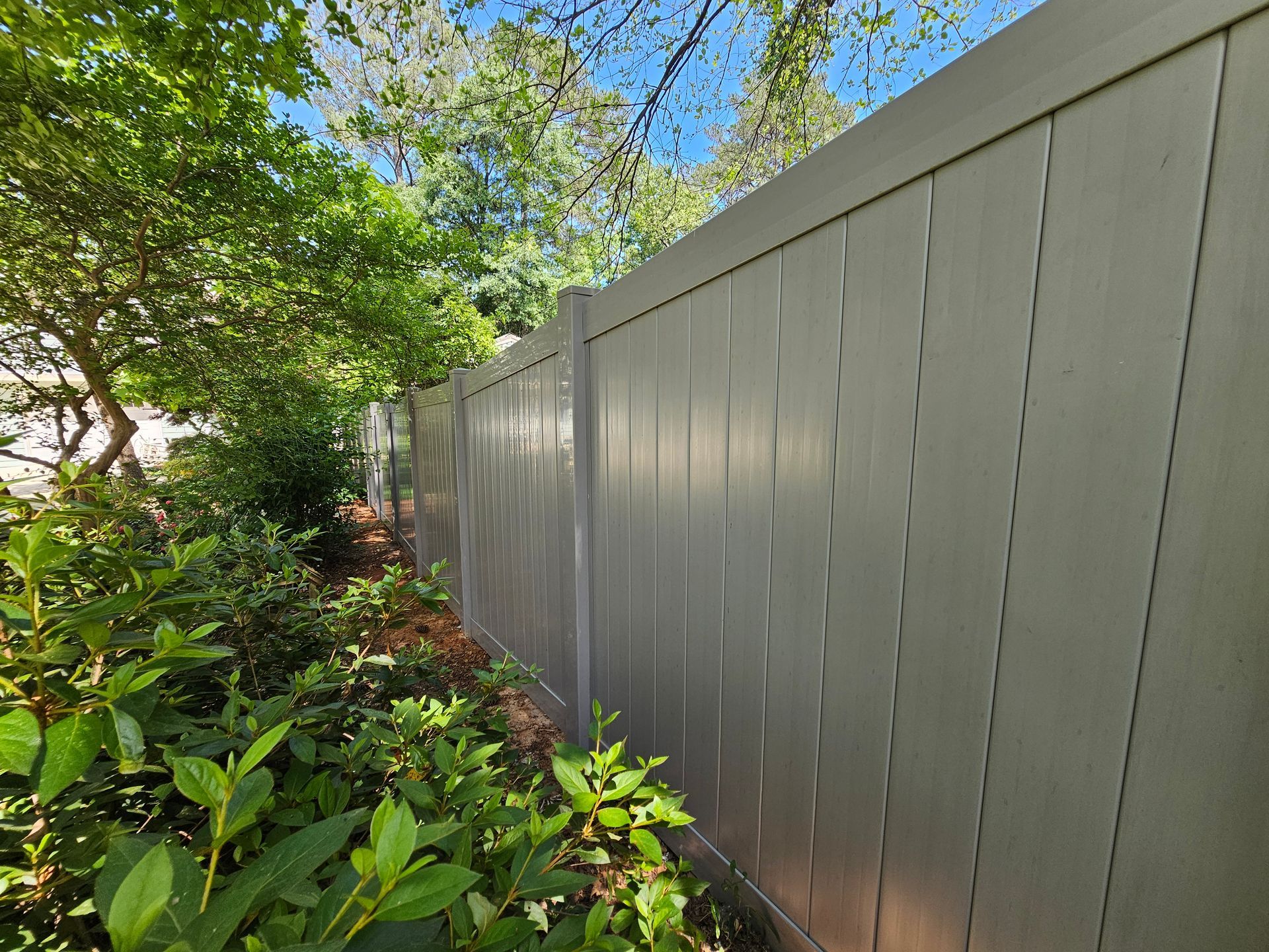 A white vinyl fence is surrounded by trees and bushes.
