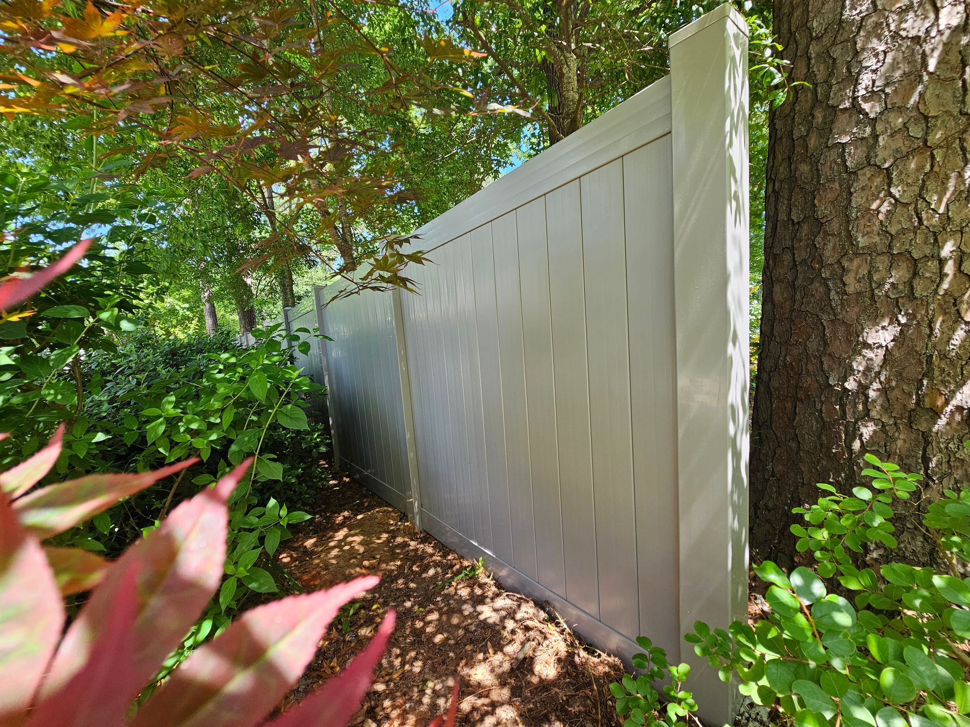A white fence is surrounded by trees and plants in a garden.
