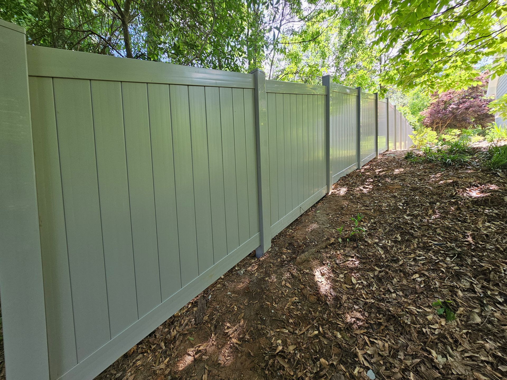 A white vinyl fence is surrounded by trees and leaves.