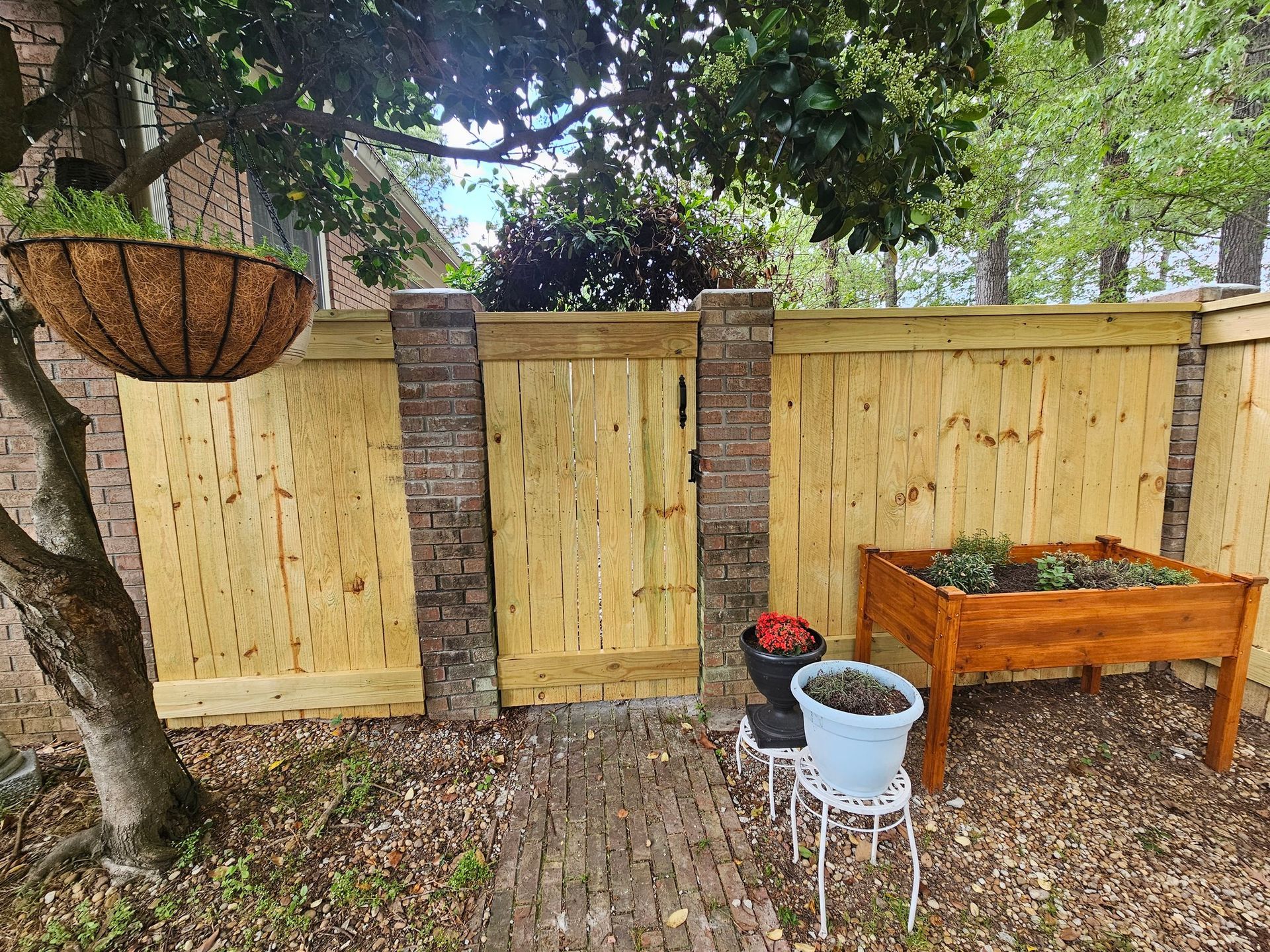 A white gate is sitting in the middle of a driveway next to a brick wall.