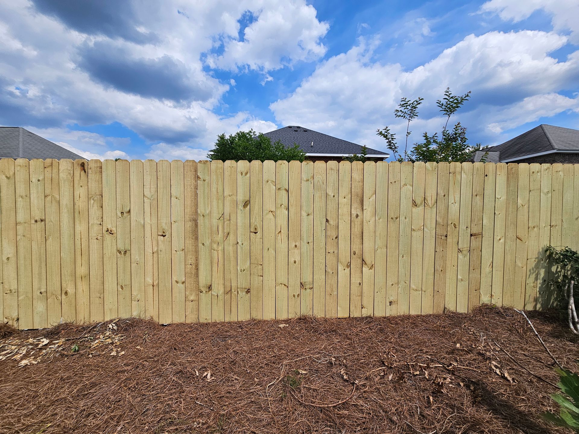 A wooden fence surrounds a pile of mulch in a backyard.