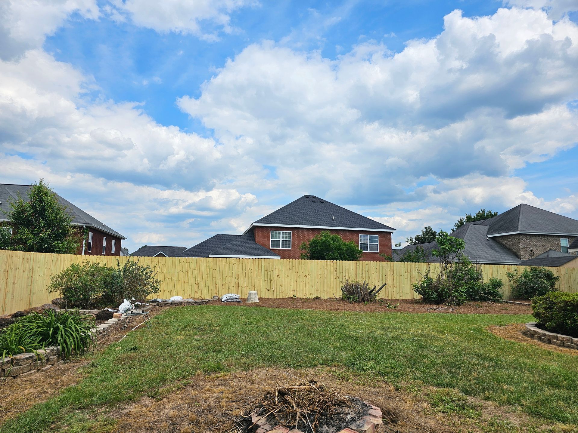A backyard with a wooden fence and a fire pit.