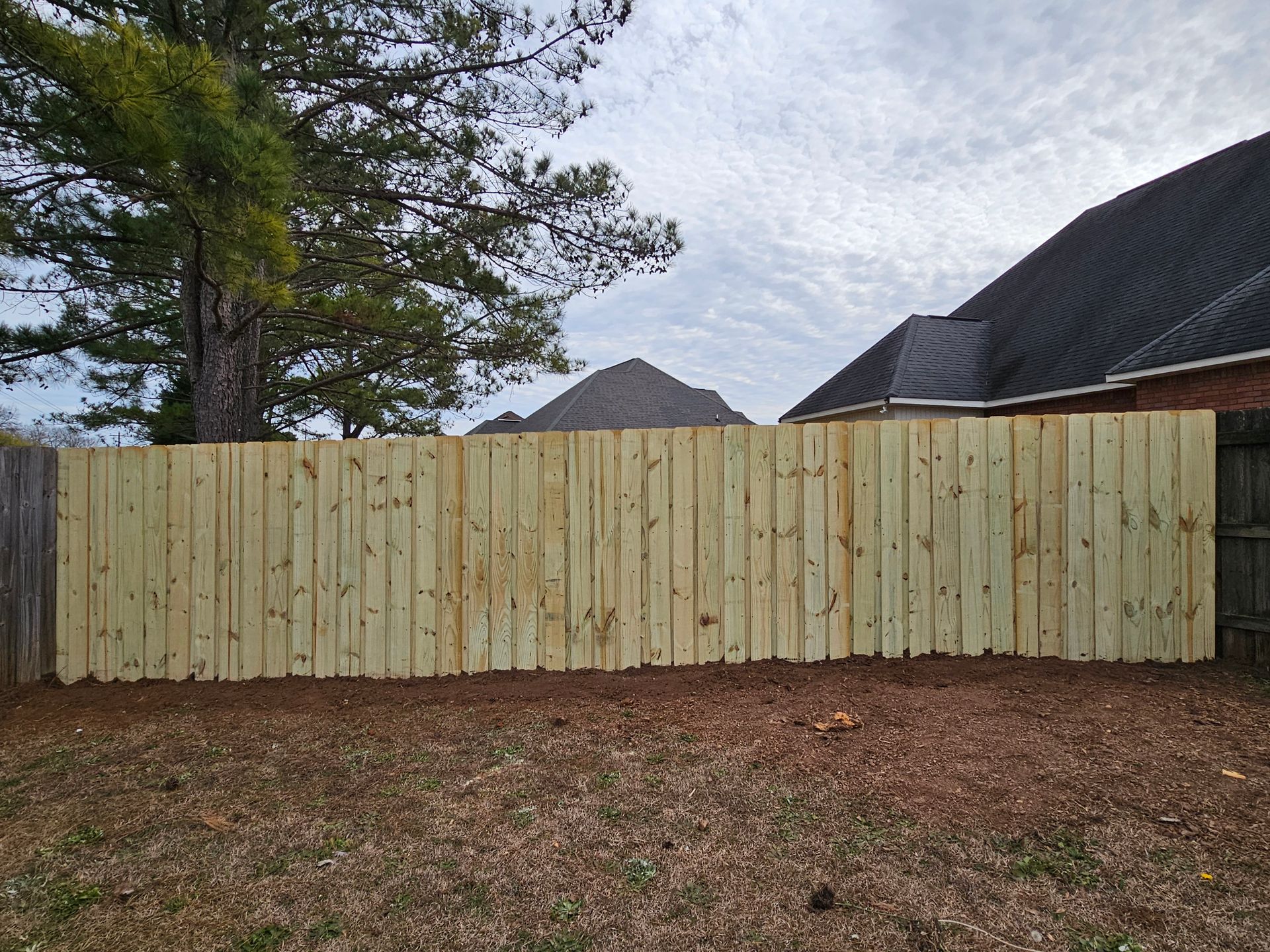 A wooden fence is in the backyard of a house.