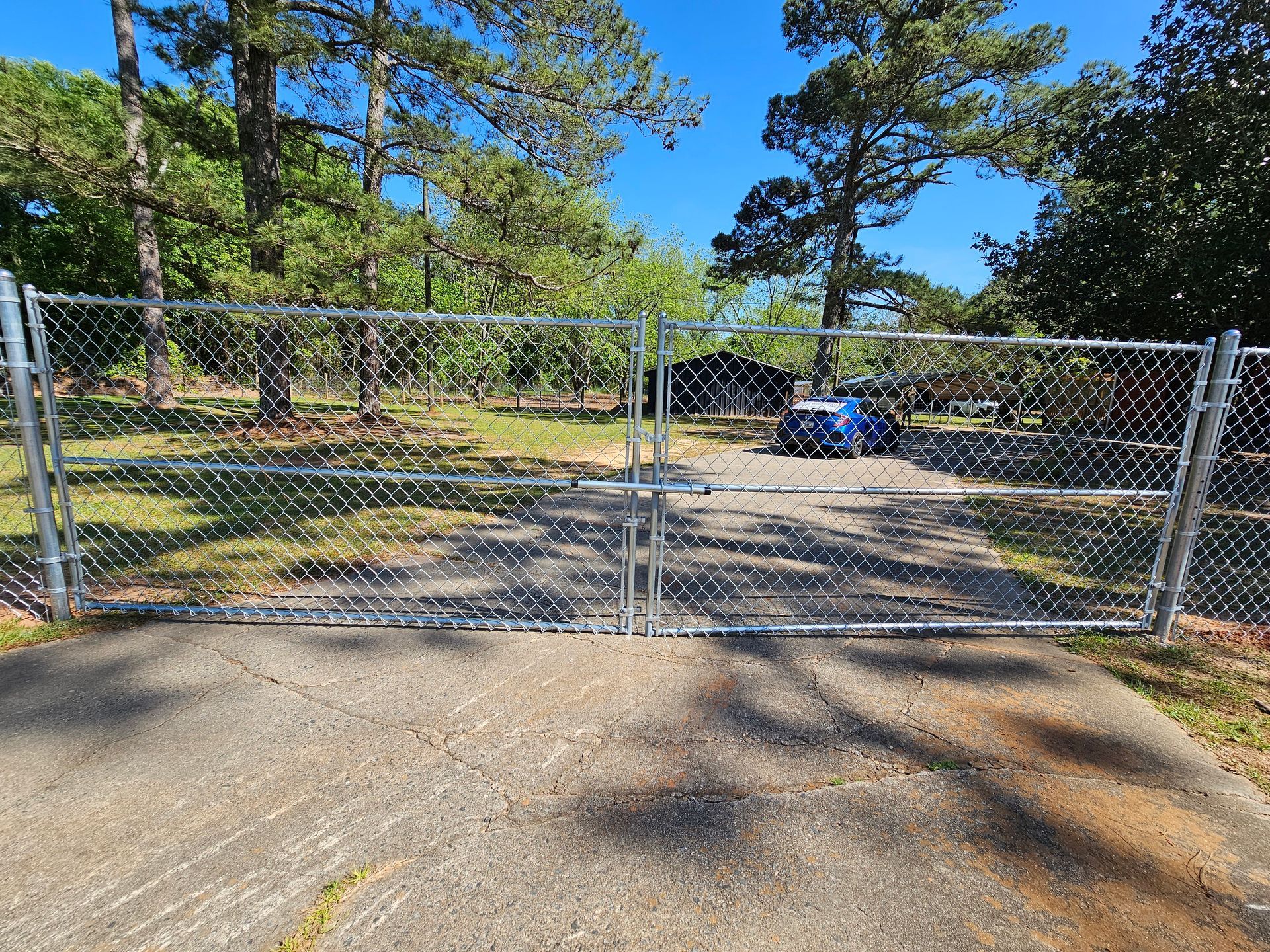 A chain link fence surrounds a driveway with trees in the background.