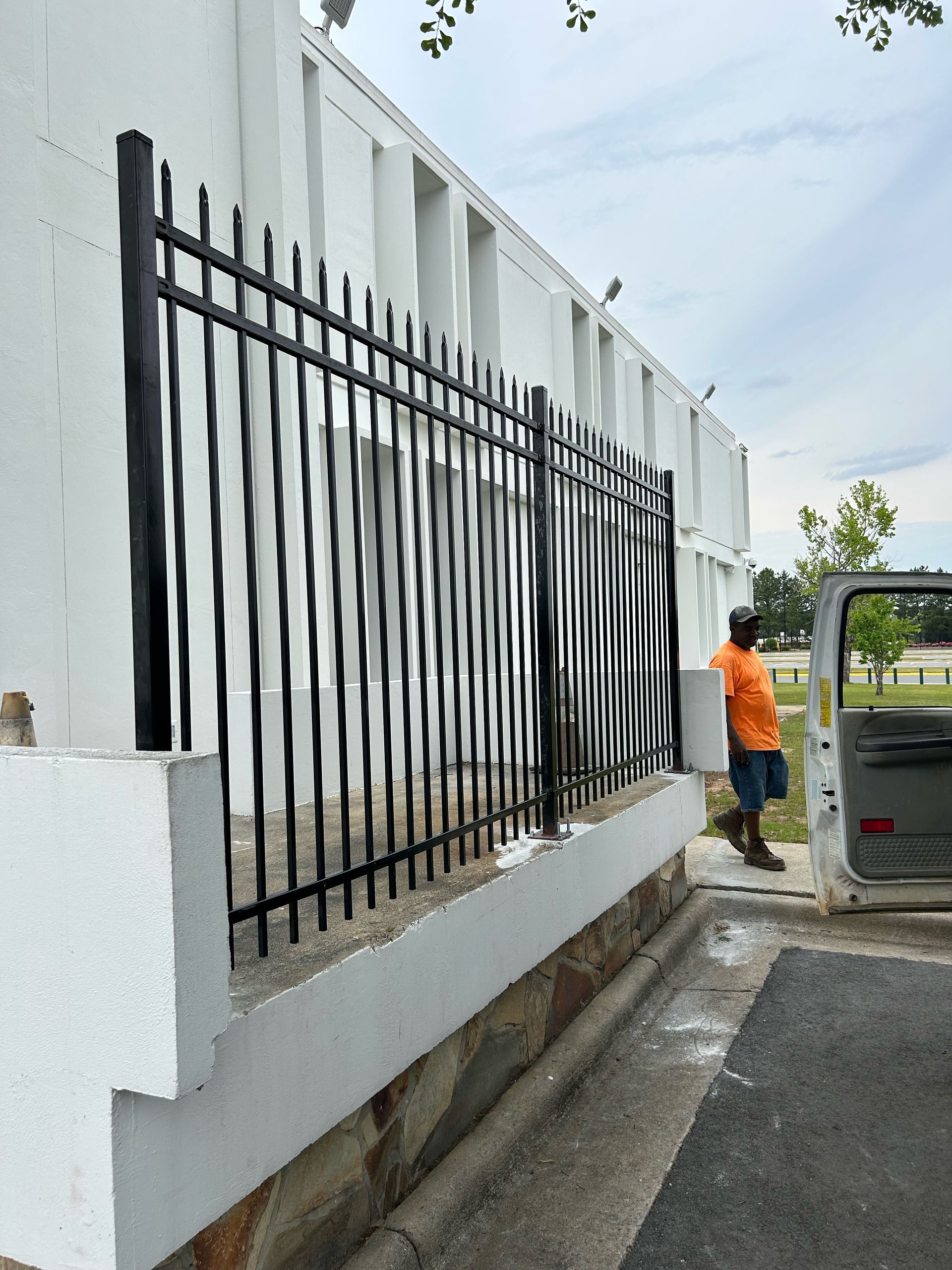 A man in an orange shirt is standing next to a fence