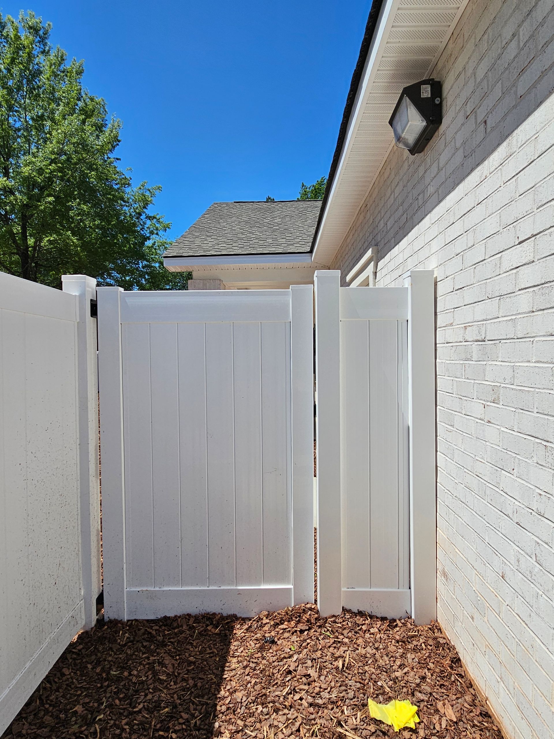 A white fence is surrounded by a brick wall and a pile of mulch.