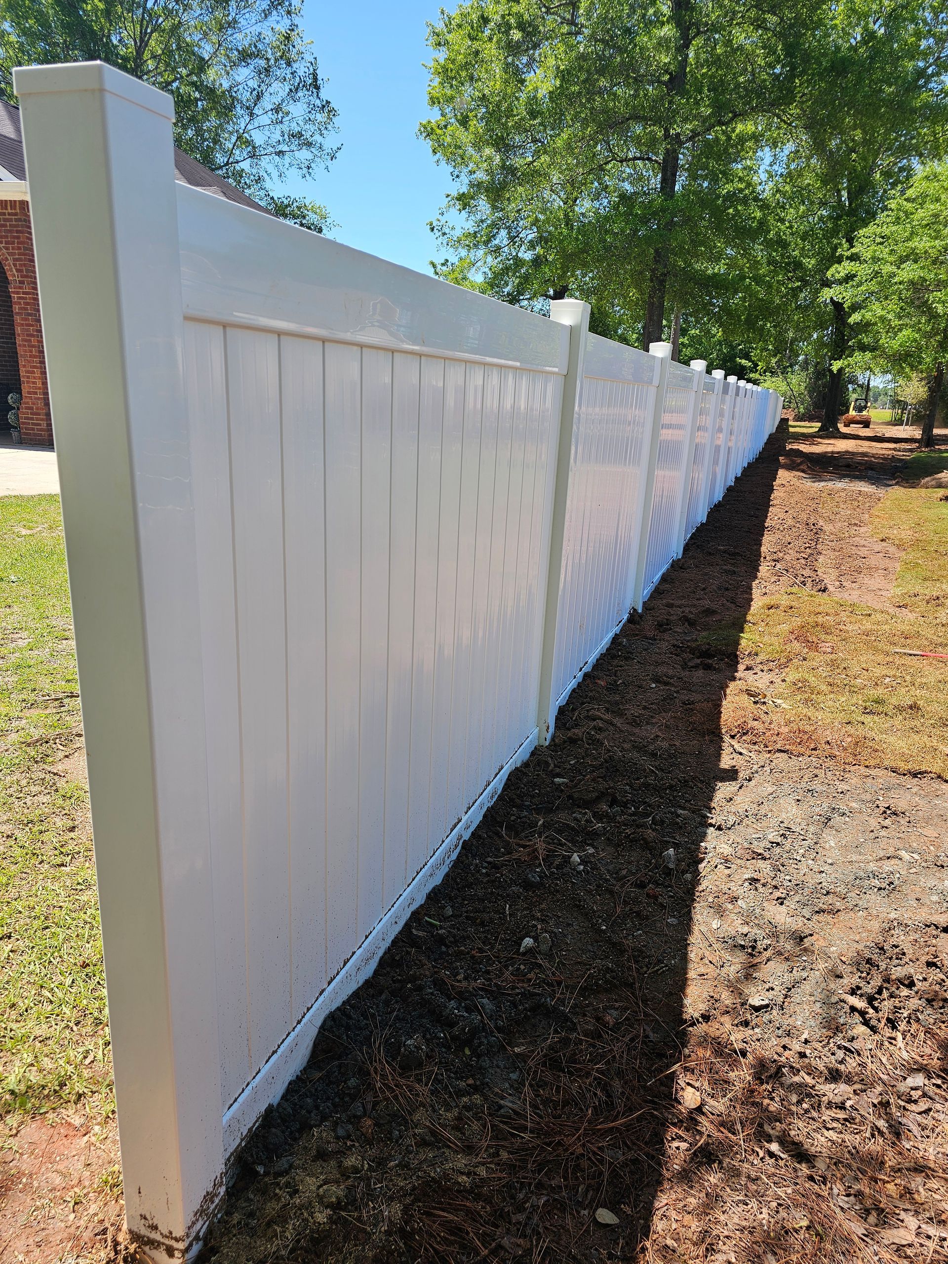 A white vinyl fence is sitting in the middle of a dirt field.
