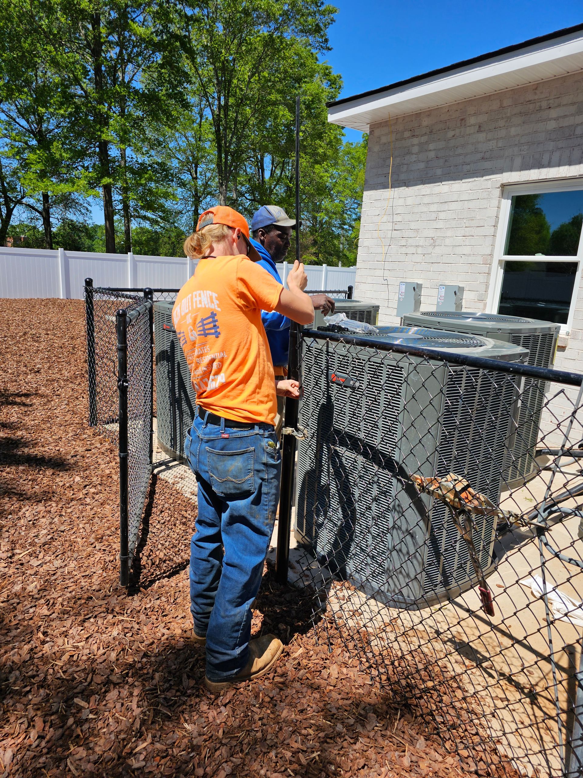 Two men are working on an air conditioner outside of a house.