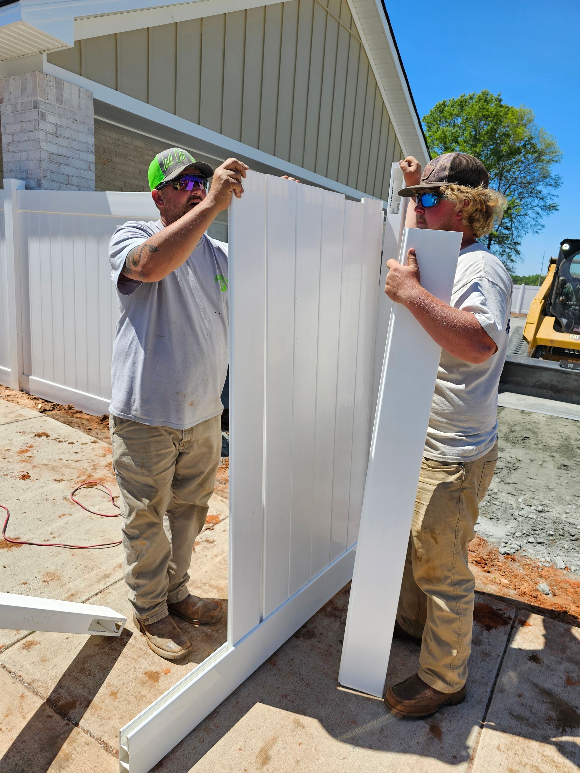 Two men are installing a white fence in front of a house.