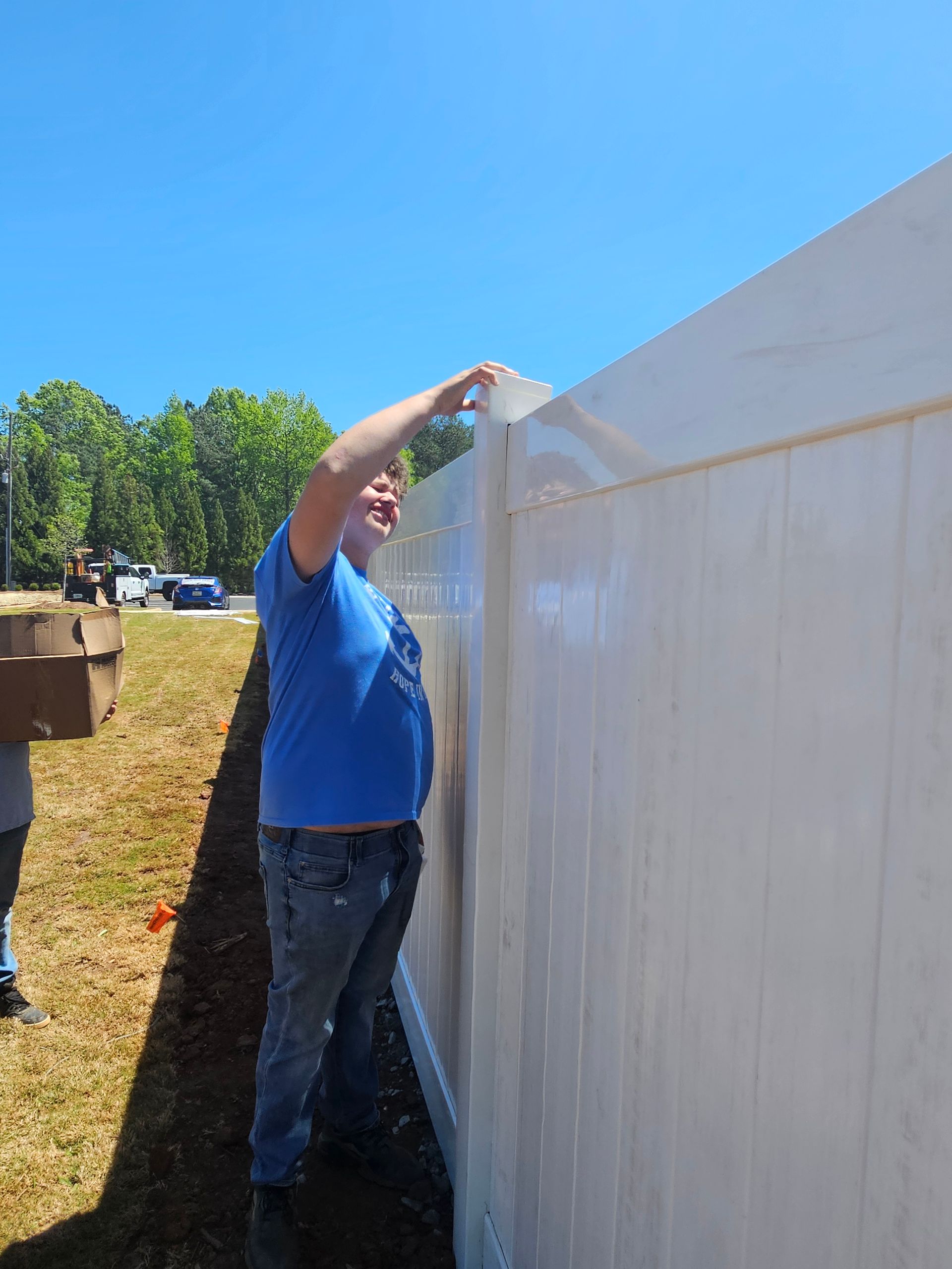 A man in a blue shirt is standing next to a white fence.