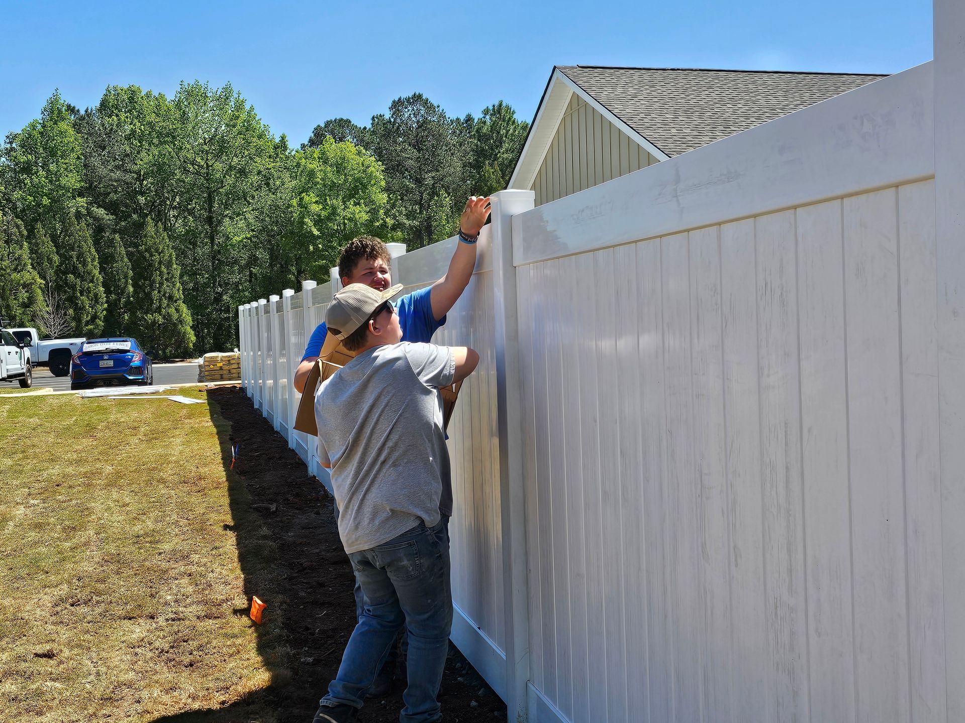 Two men are working on a white fence in front of a house.