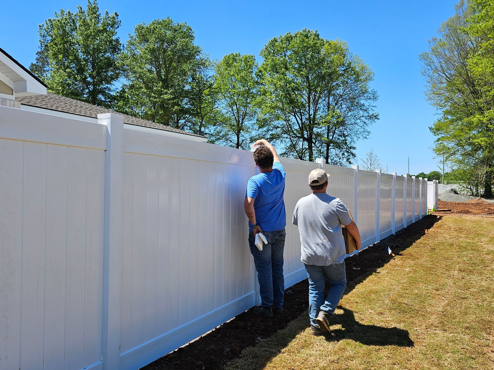 Two men are painting a white fence in a yard.