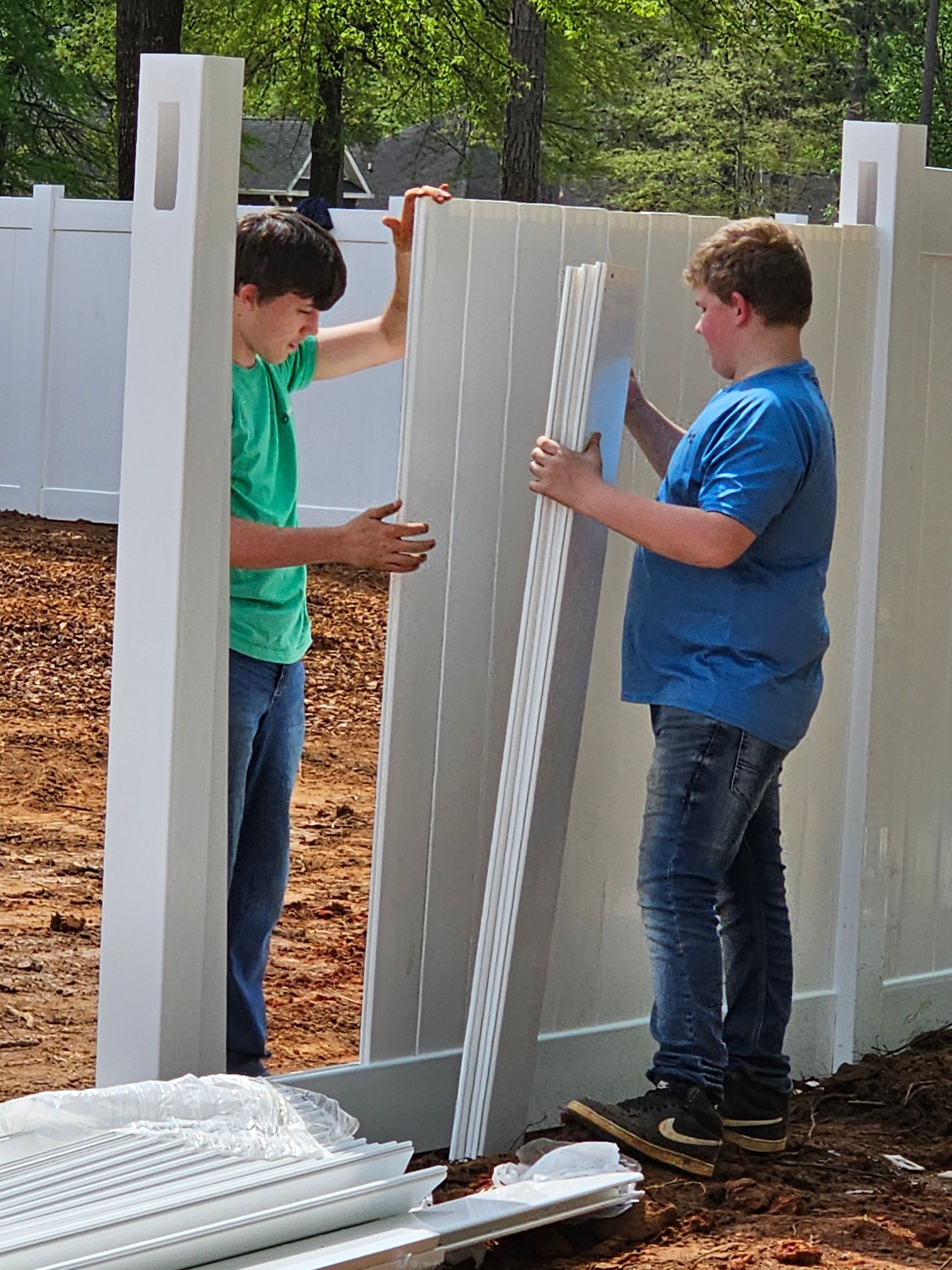Two young men are working on a white fence.