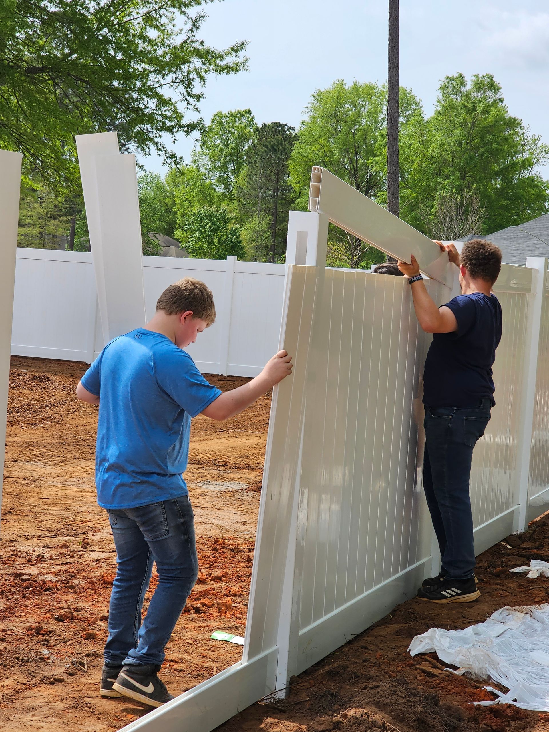 Two men are installing a white fence in a yard.