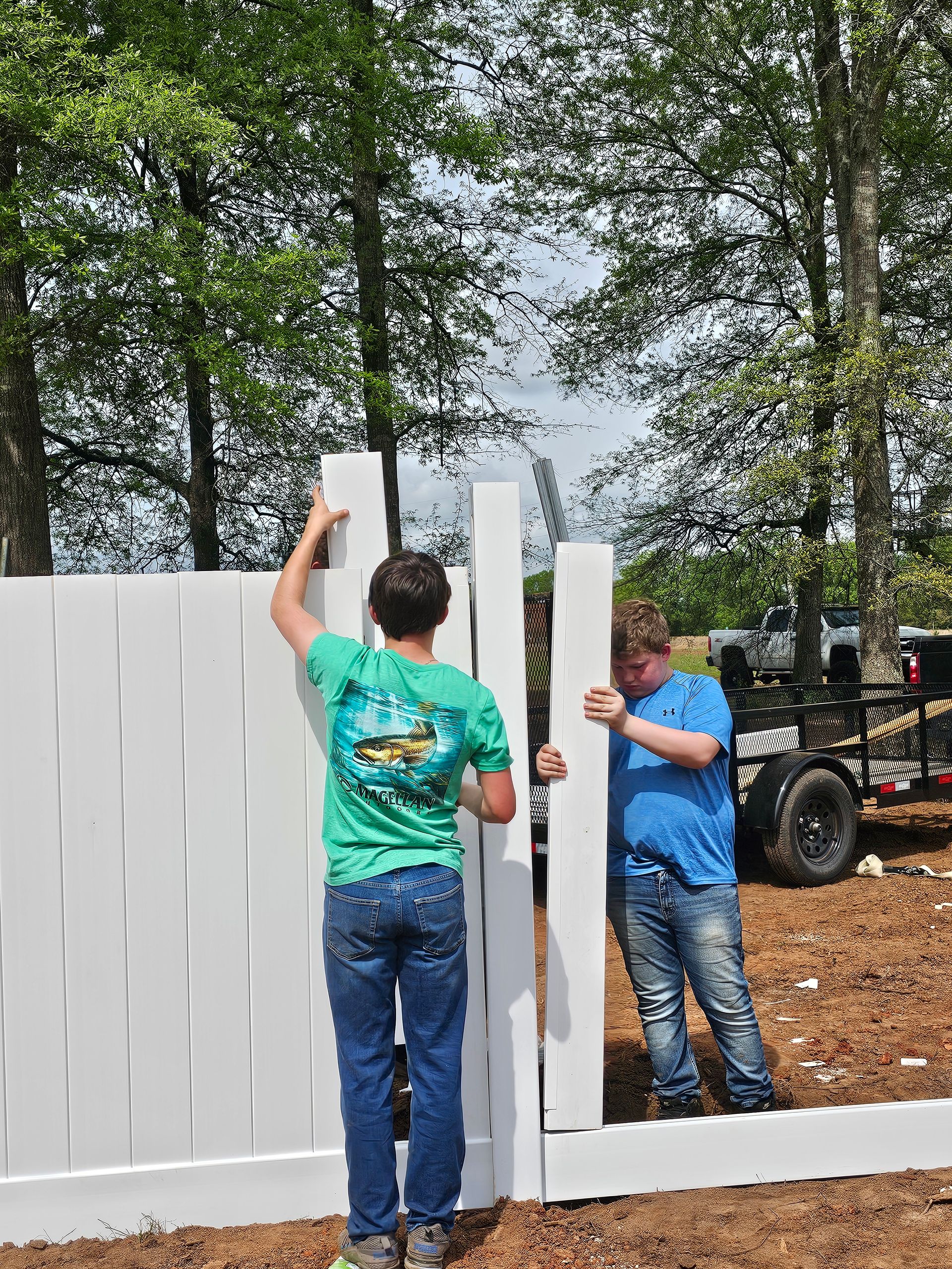 Two men are working on a white fence.