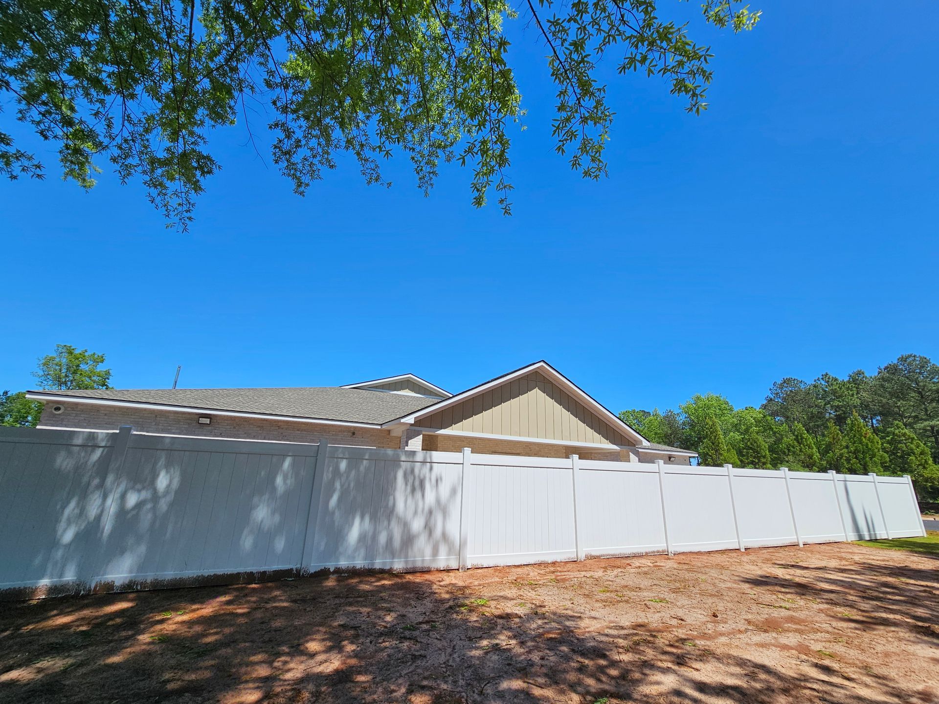A white fence surrounds a dirt field in front of a house.