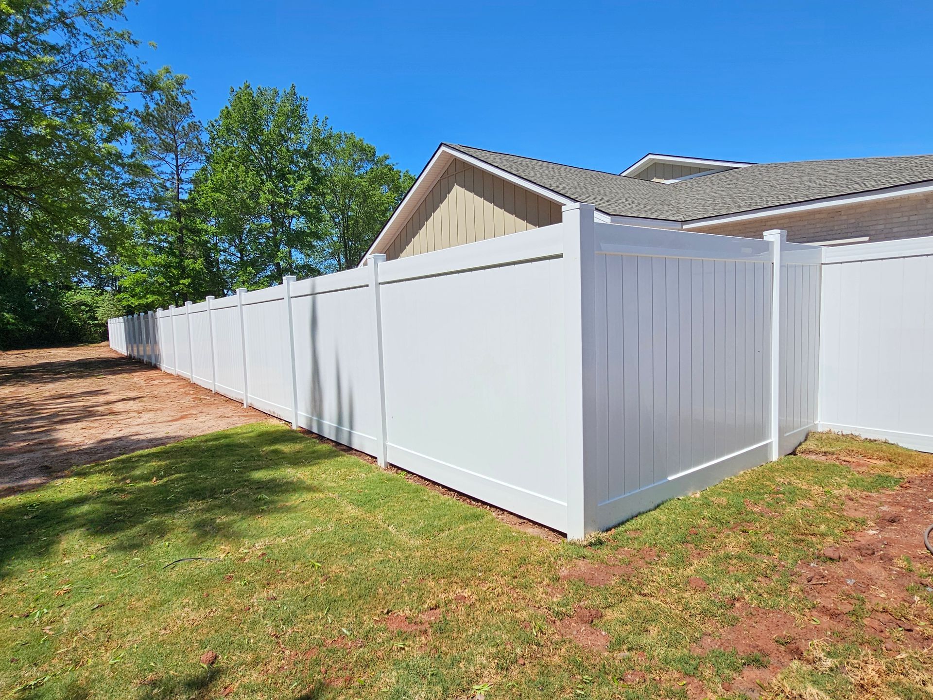 A white vinyl fence is in the backyard of a house.