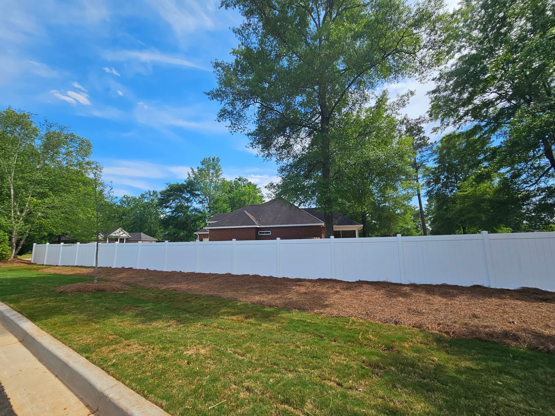 A white fence surrounds a lush green field in front of a house.