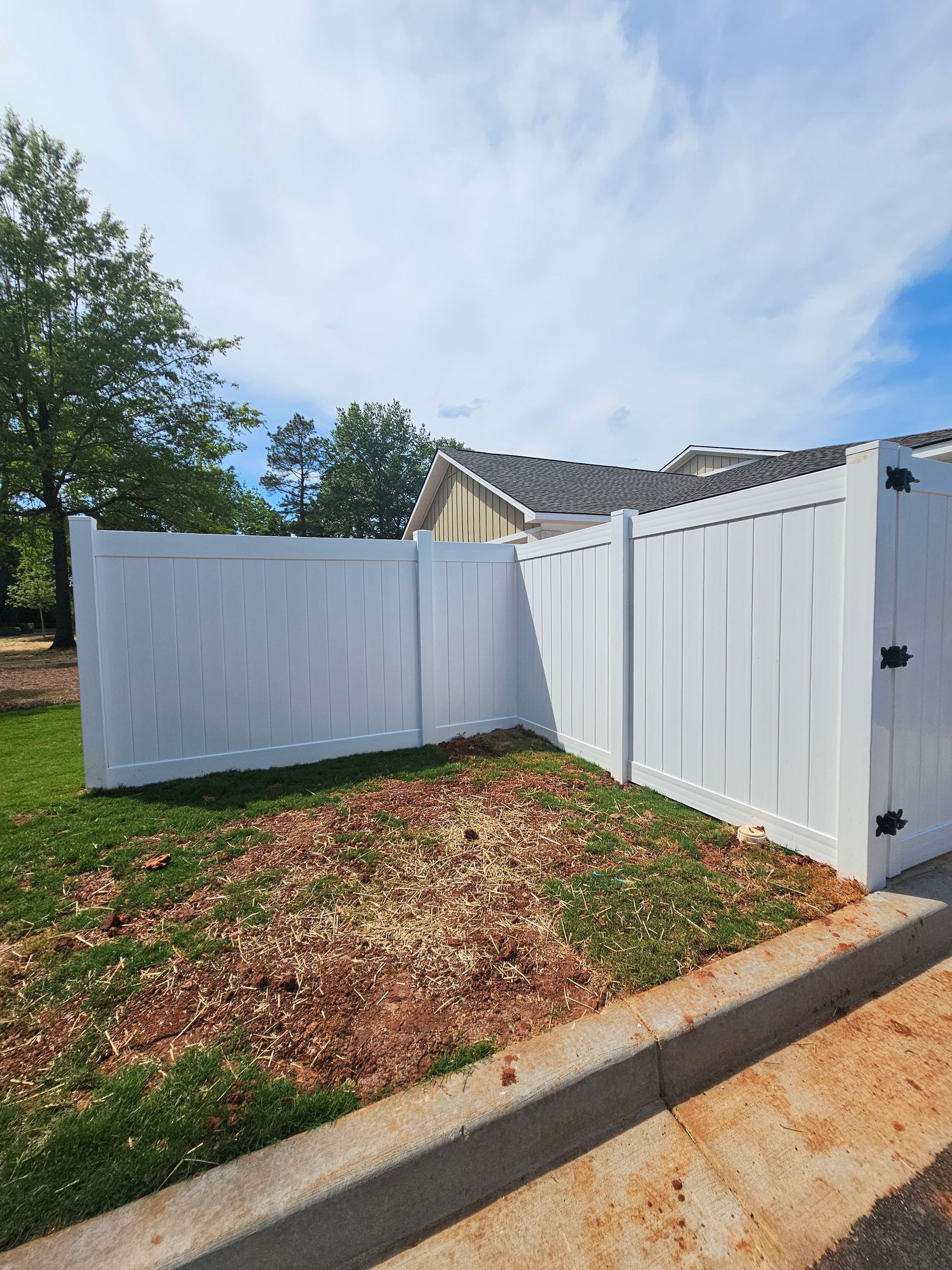 A white fence is sitting on the side of a road in front of a house.