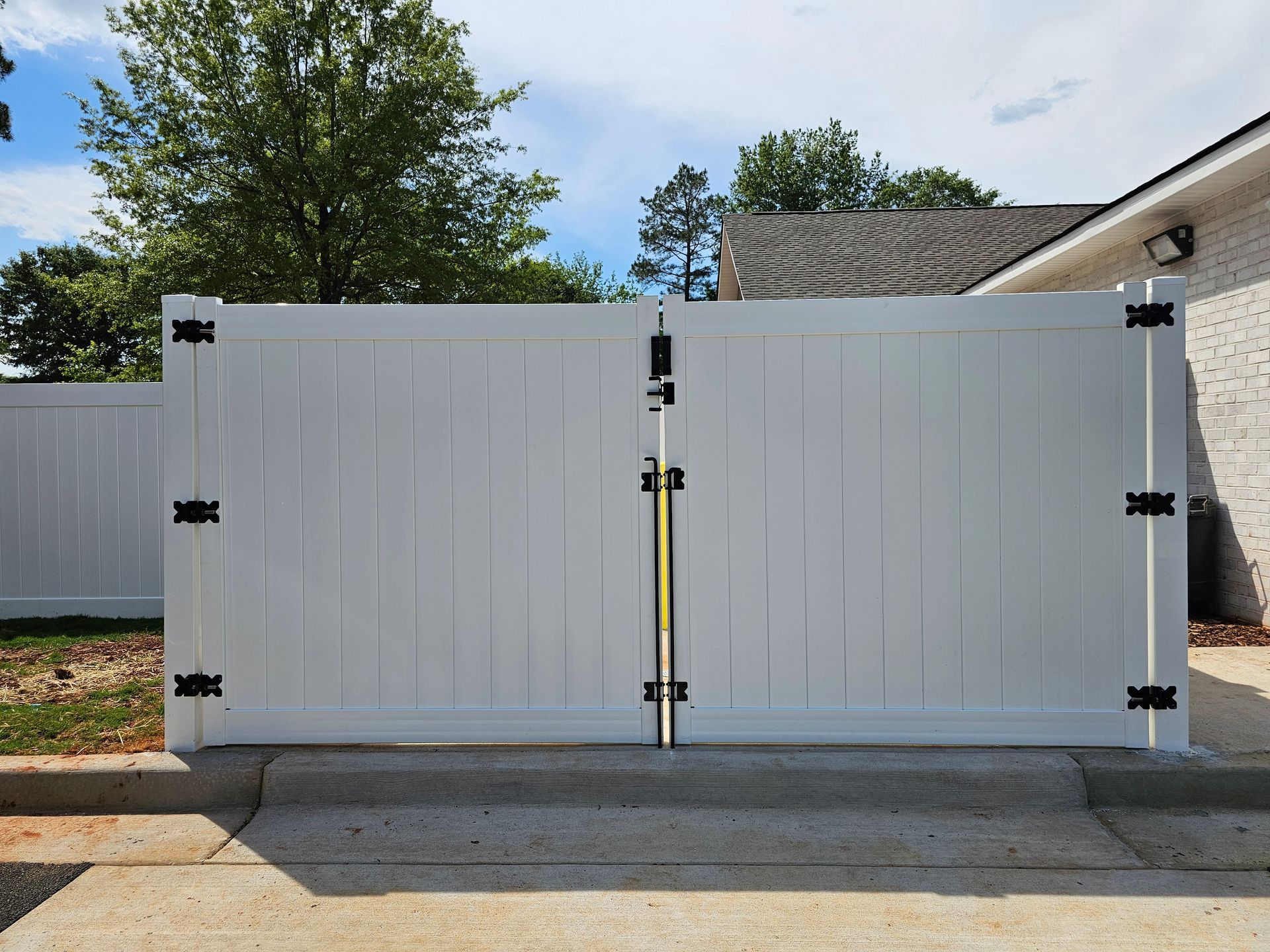 A white fence is sitting on the side of the road in front of a house.