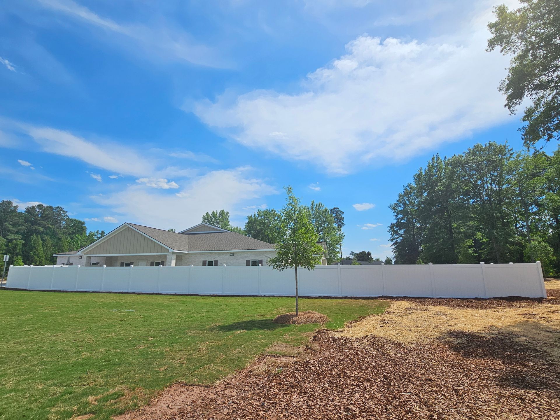 A white fence surrounds a house in a grassy field.