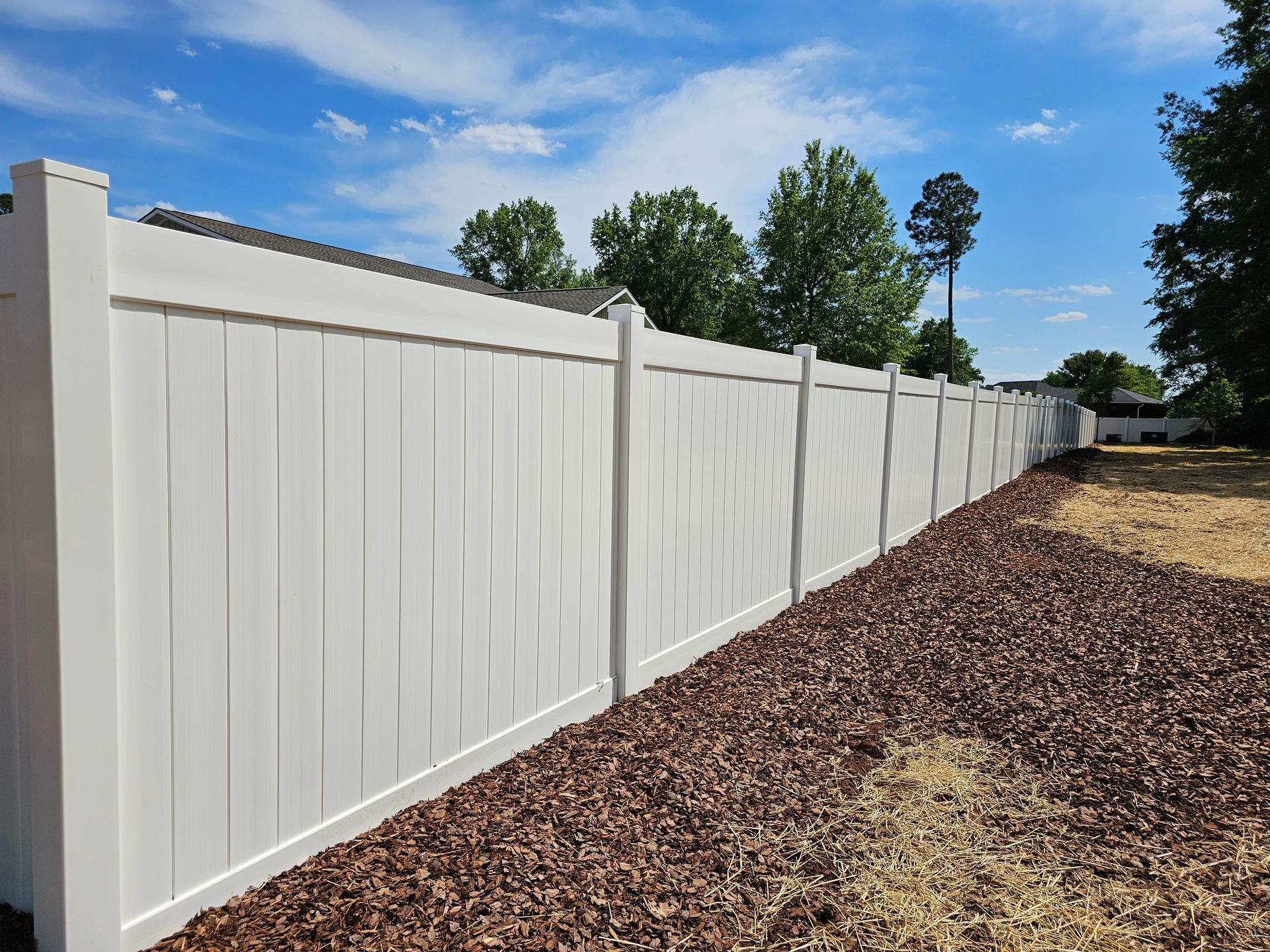 A white vinyl fence surrounds a yard with trees in the background.