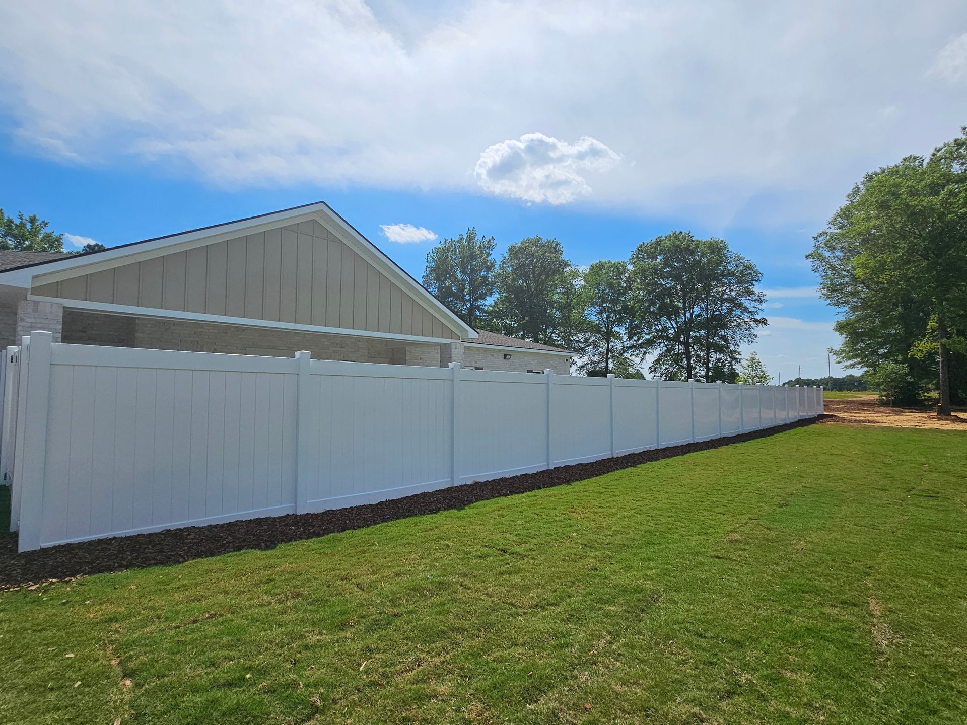 A white fence surrounds a lush green field in front of a house.