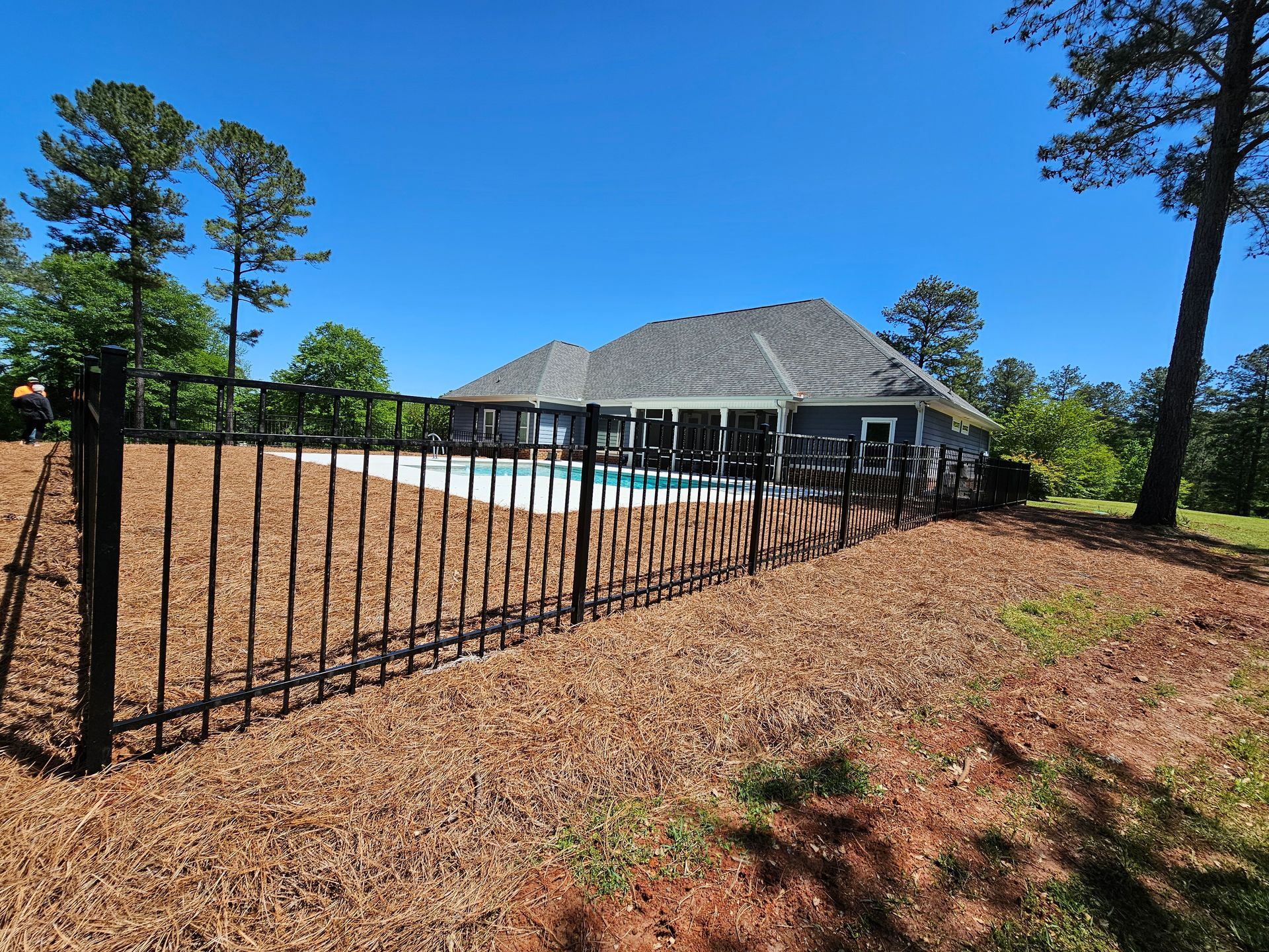 A black fence surrounds a swimming pool in front of a house.