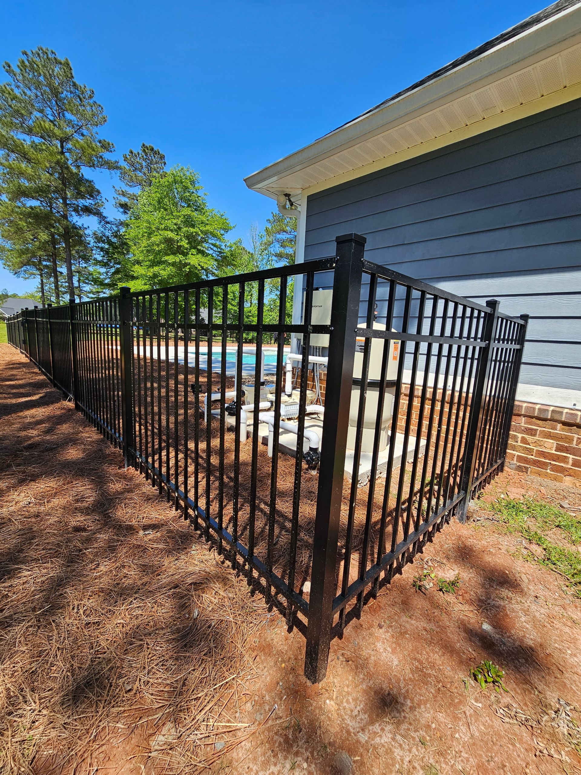 A black metal fence surrounds a swimming pool in front of a house.