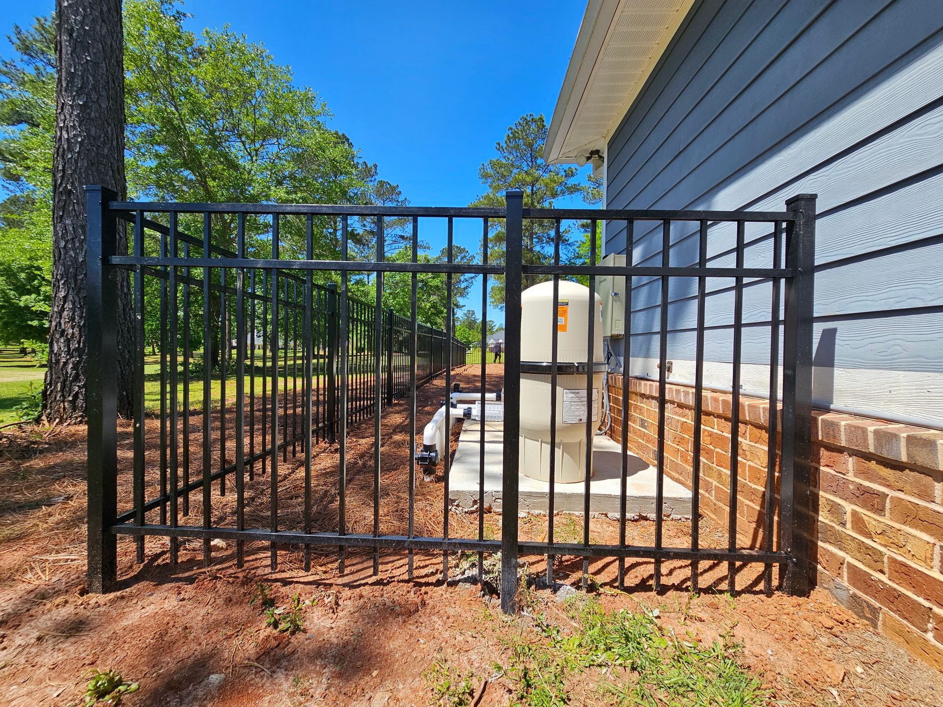 A black metal fence is surrounding a brick house.