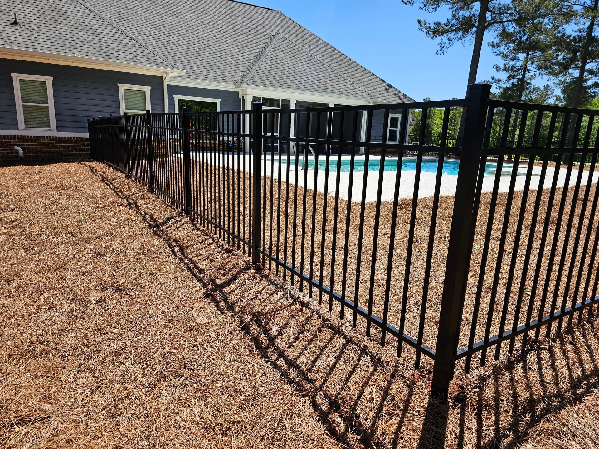 A black fence surrounds a swimming pool in front of a house