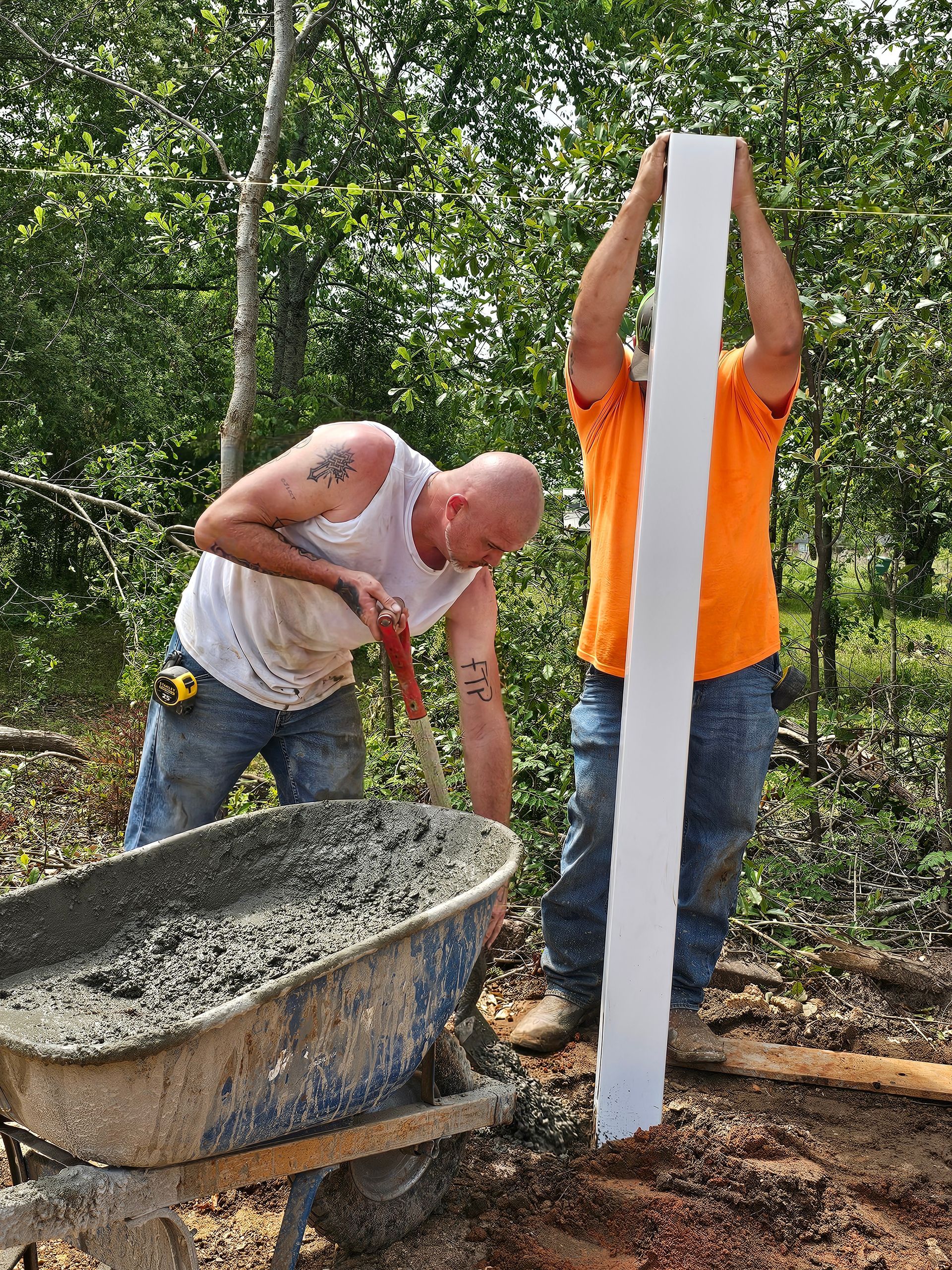 Two men are standing next to a wheelbarrow filled with concrete.