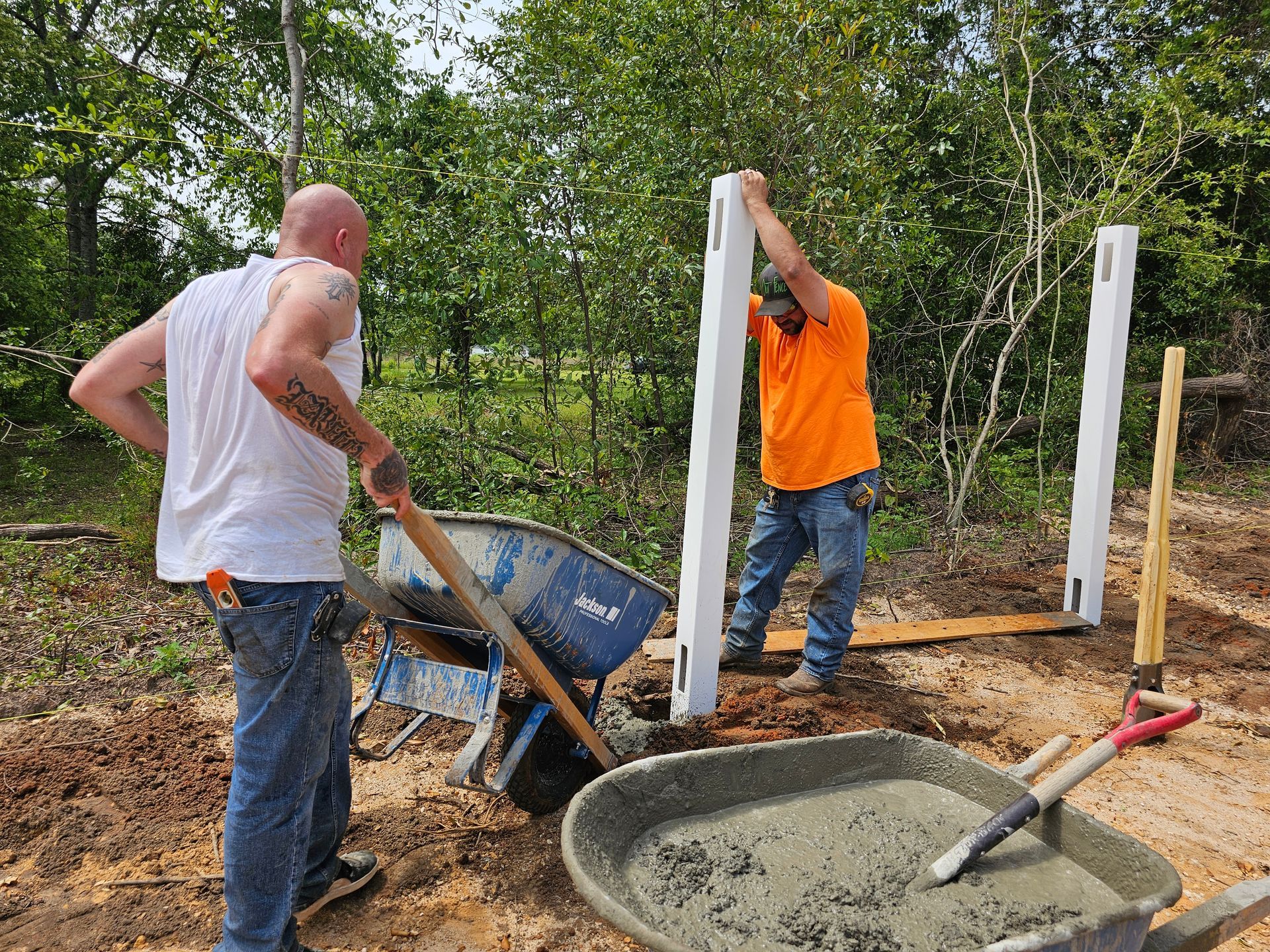Two men are standing next to a wheelbarrow filled with concrete.