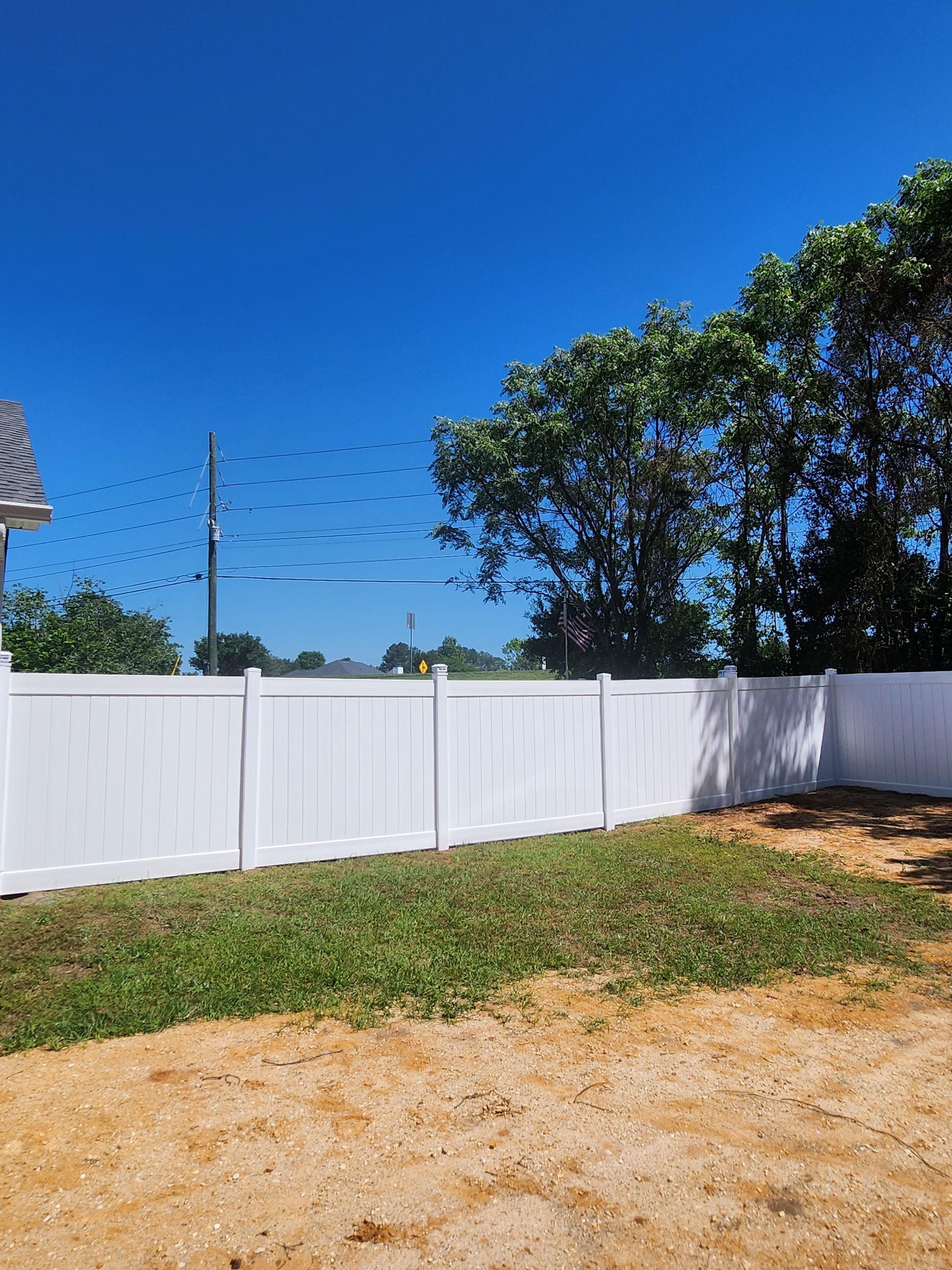 A white fence surrounds a grassy yard with trees in the background.