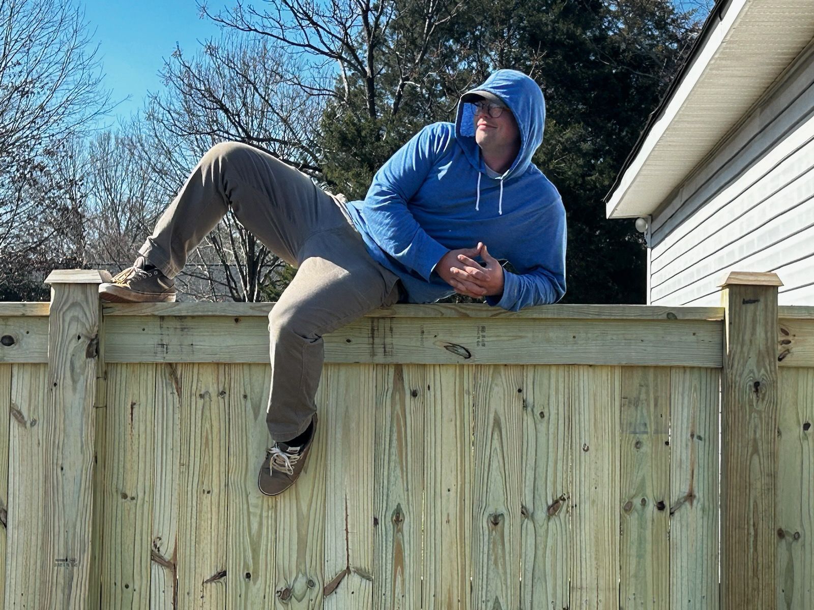 A man in a blue hoodie is sitting on a wooden fence