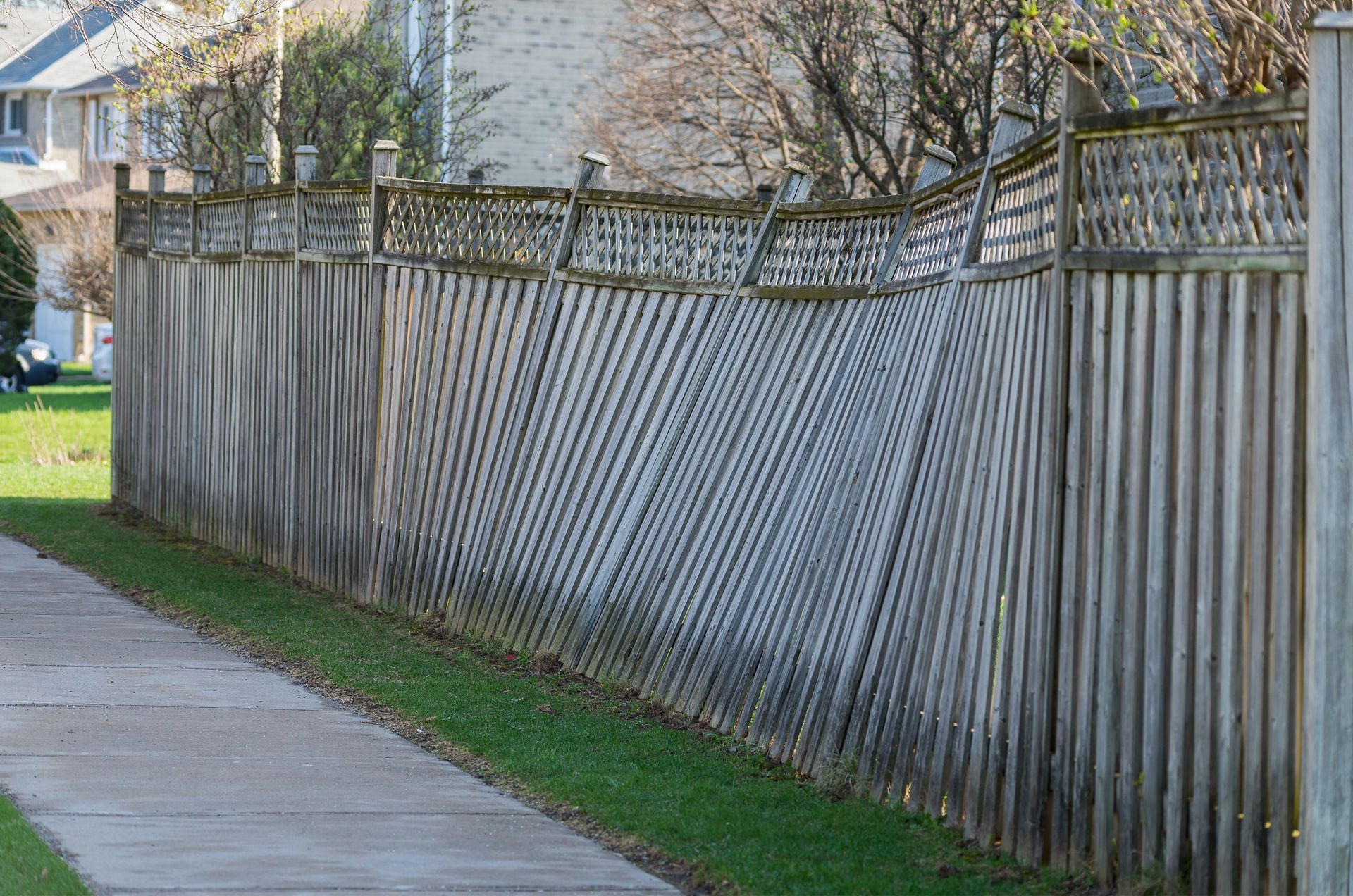 A wooden fence is along a sidewalk next to a house.