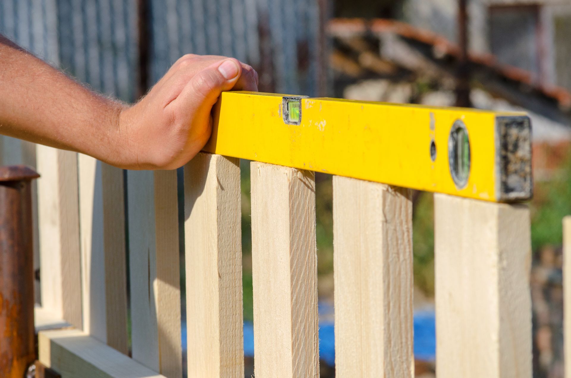 A person is measuring a wooden fence with a yellow level.
