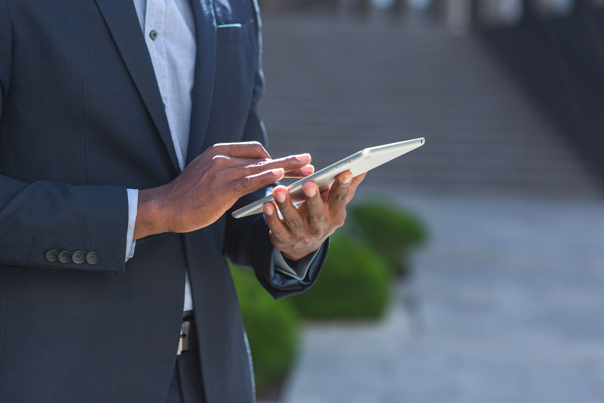 Person in a suit using a tablet outside, with a blurred background of a building.