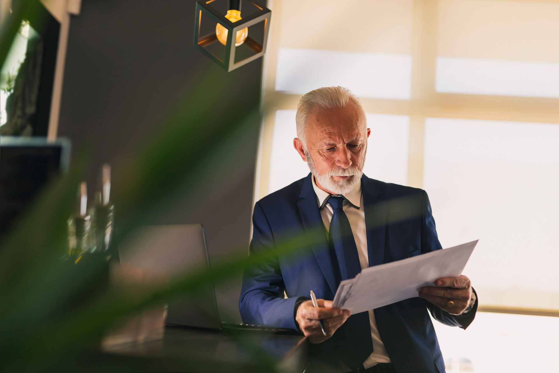 Man in blue suit, looking at documents, interior setting.