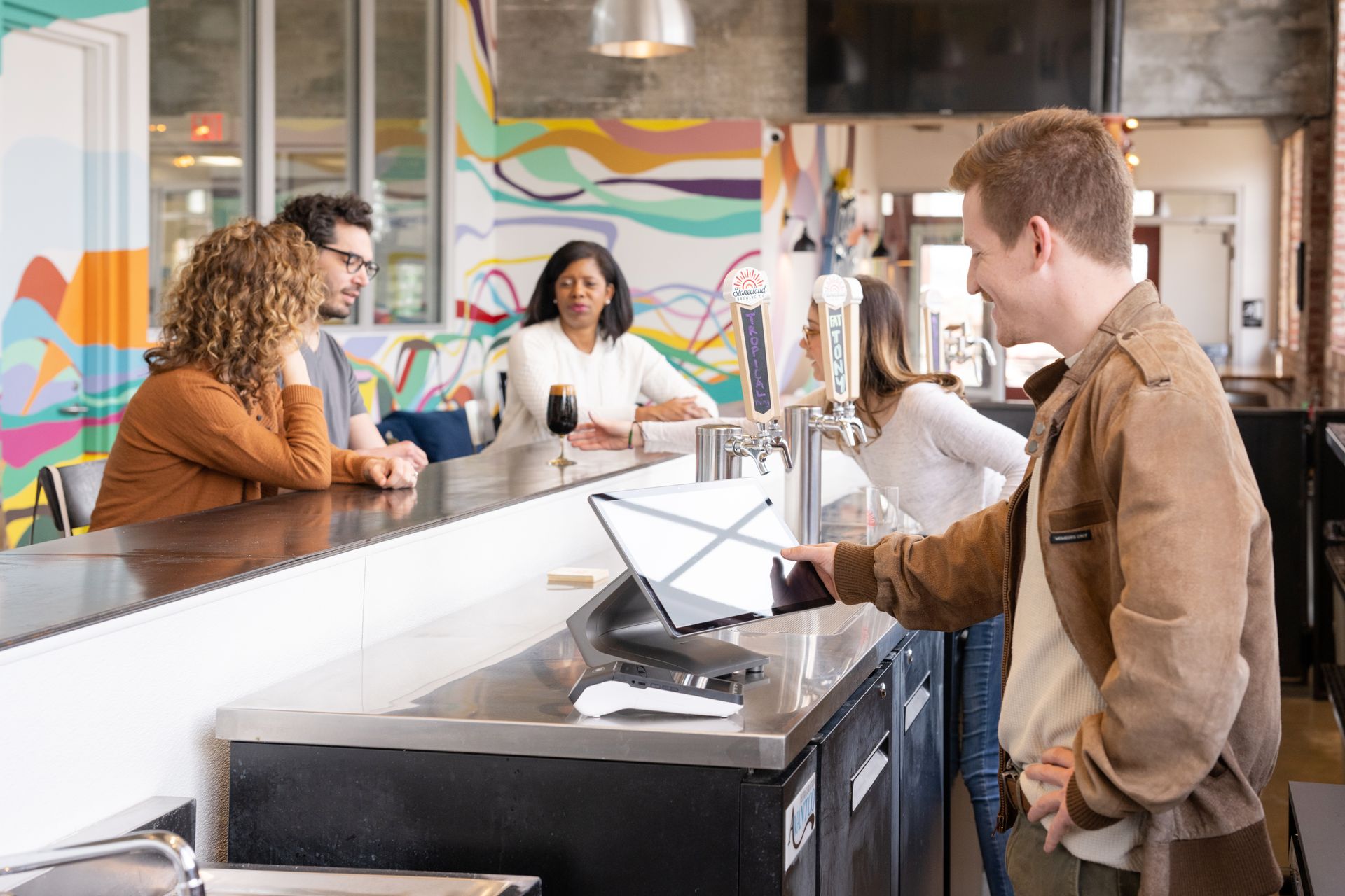 Man at bar paying with card reader, other patrons in background.