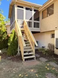 Exterior wooden stairs leading to a raised house entrance between beige siding and bushes