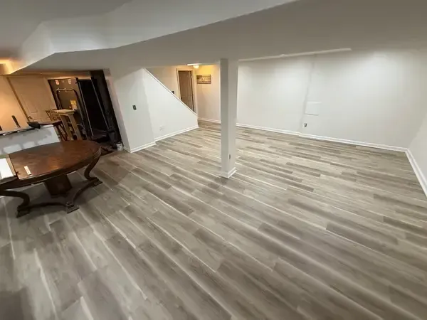 Empty open-plan living and dining room with gray wood-look floors, white walls, and a central support column